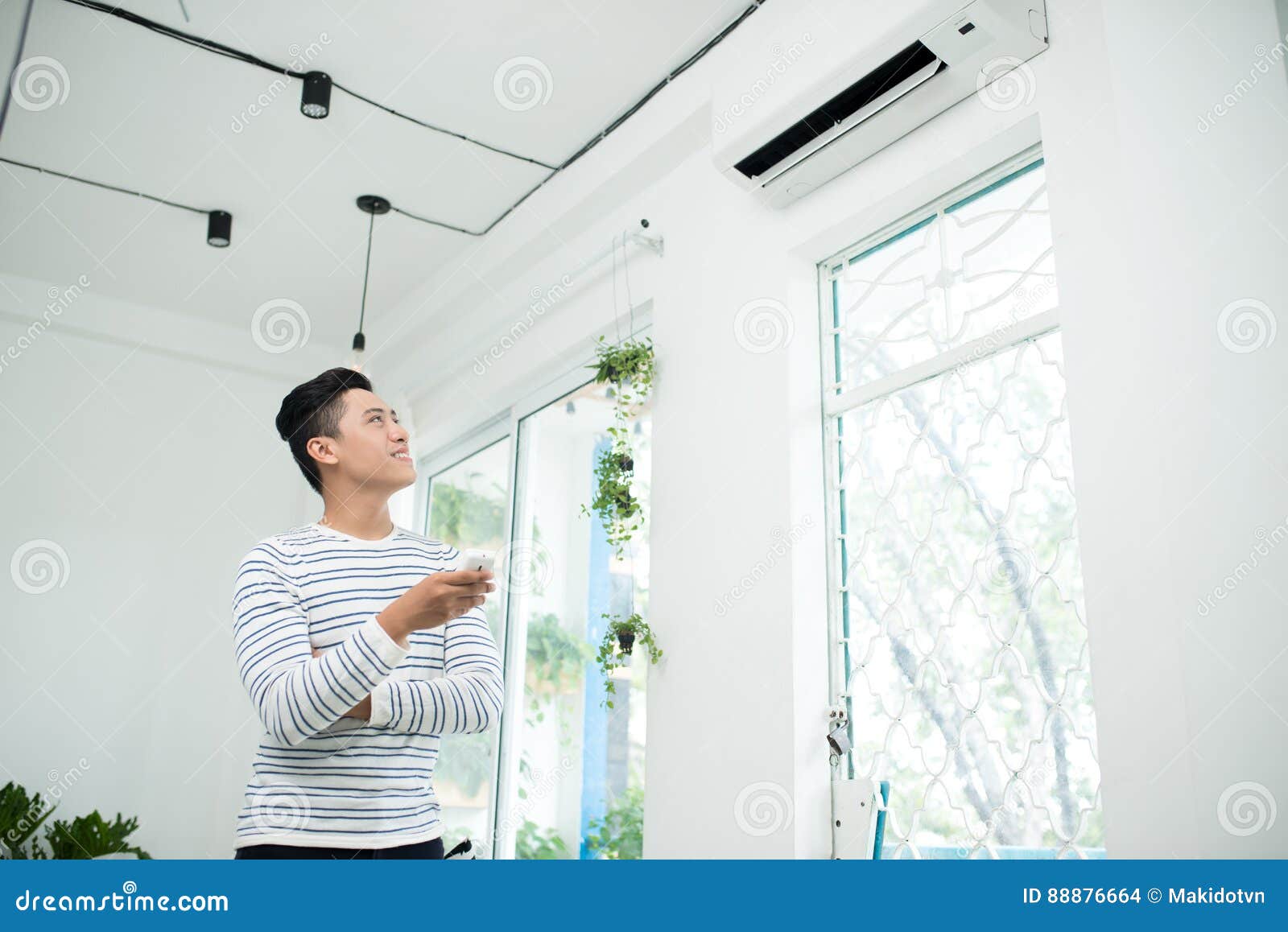 asian man is turning air condition by remote control and smiling