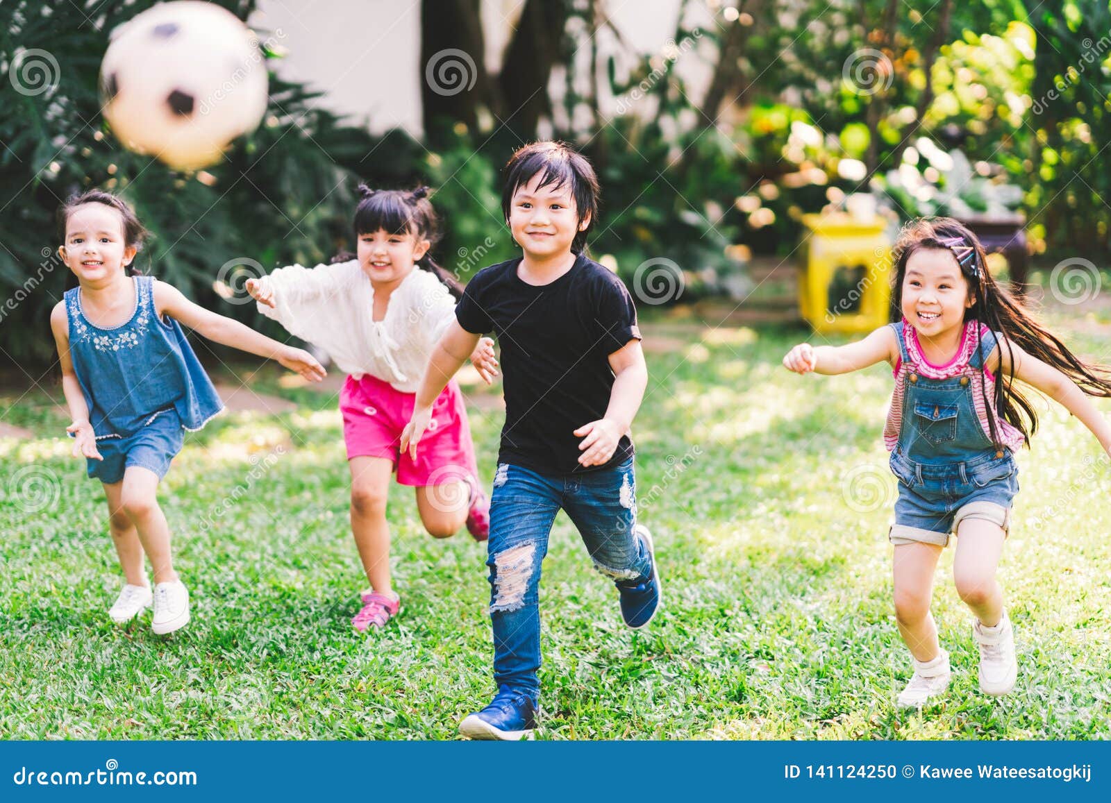 asian and mixed race happy young kids running playing football together in garden. multi-ethnic children group, outdoor exercising