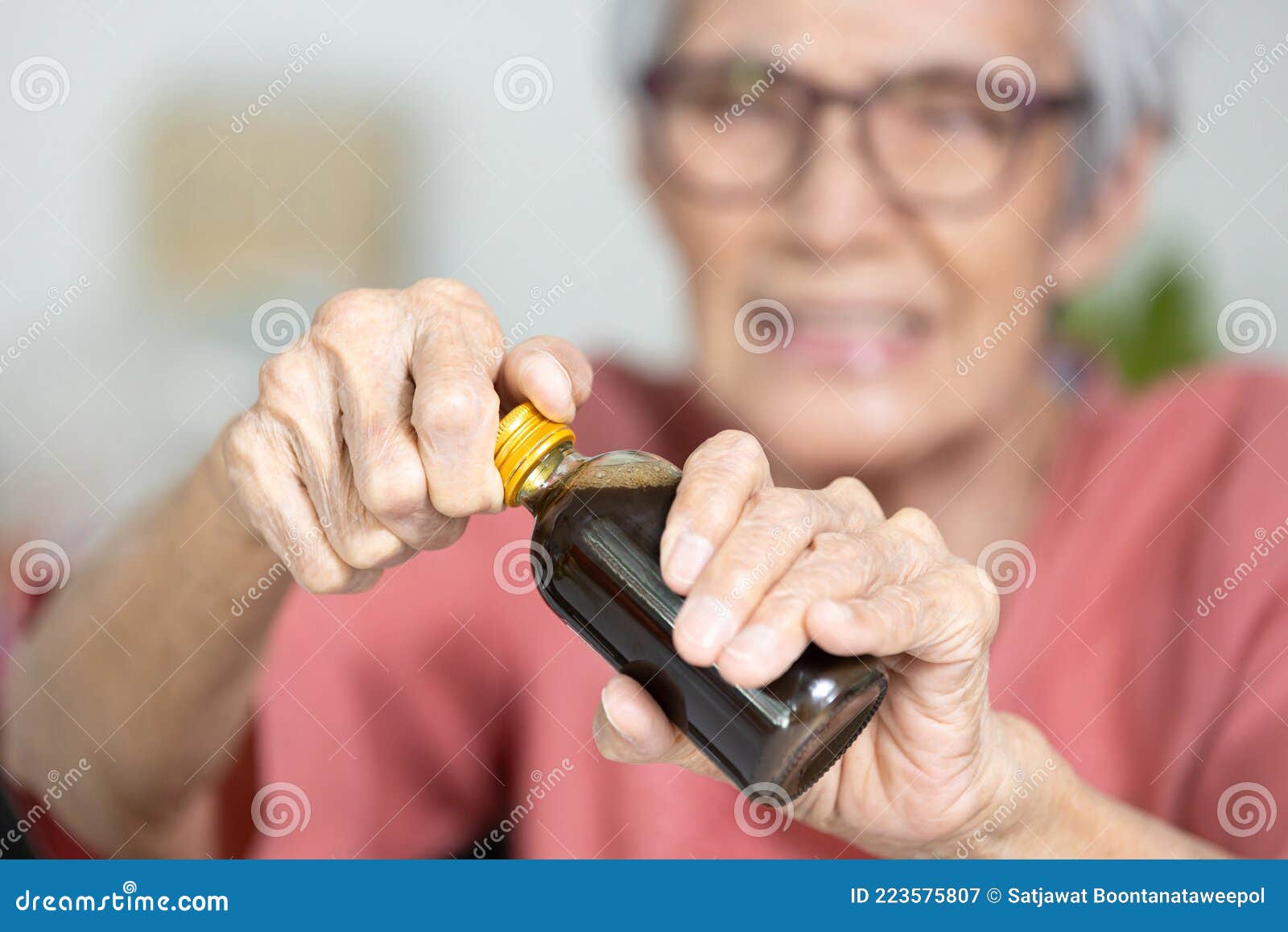 asian senior woman hold a bottle of liquid drug,old elderly try to open the screw cap of bottle with difficulty,unscrew cap to