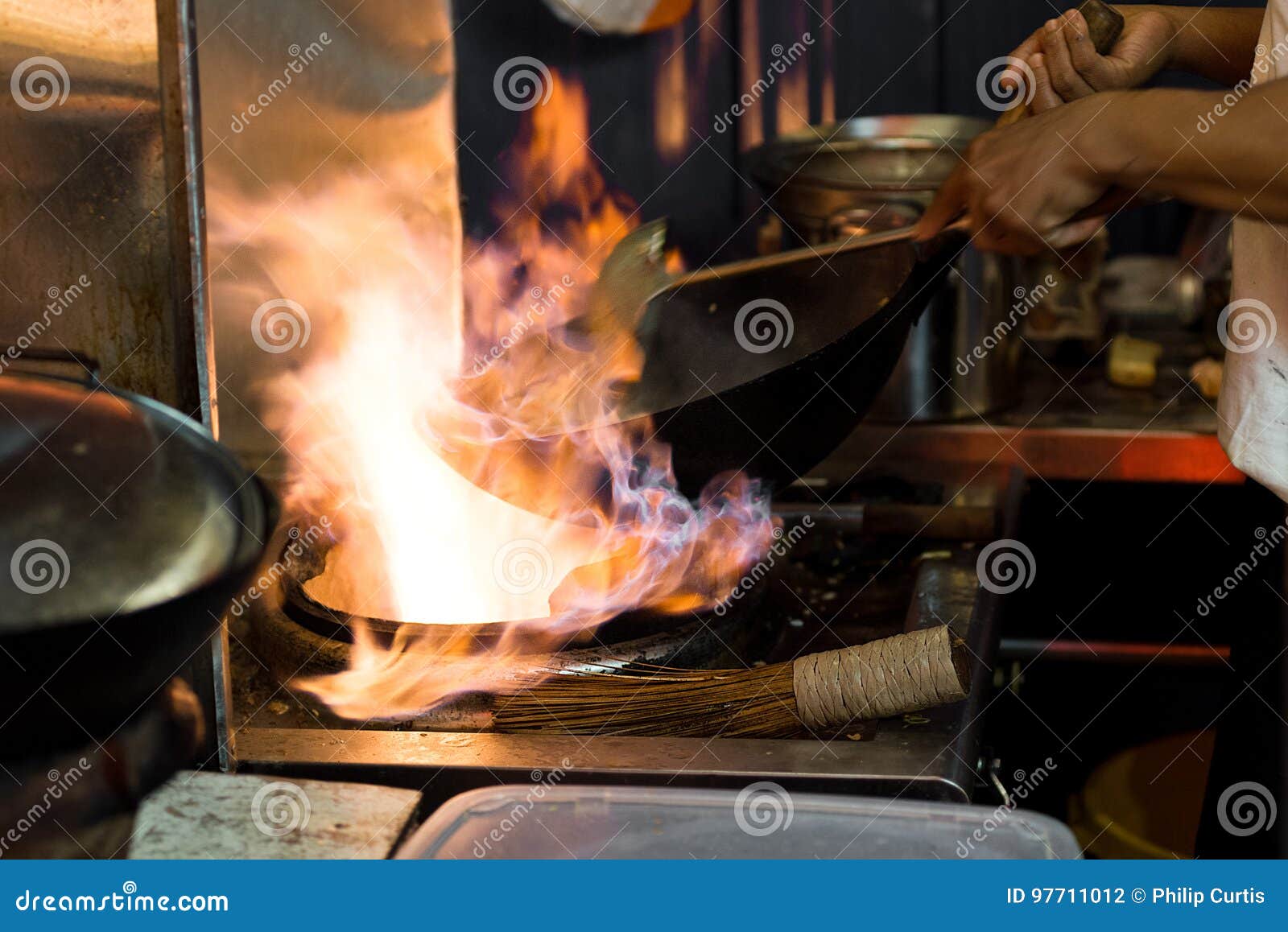 Unrecognizable man cooking in fatiscent big pan or wok in a small