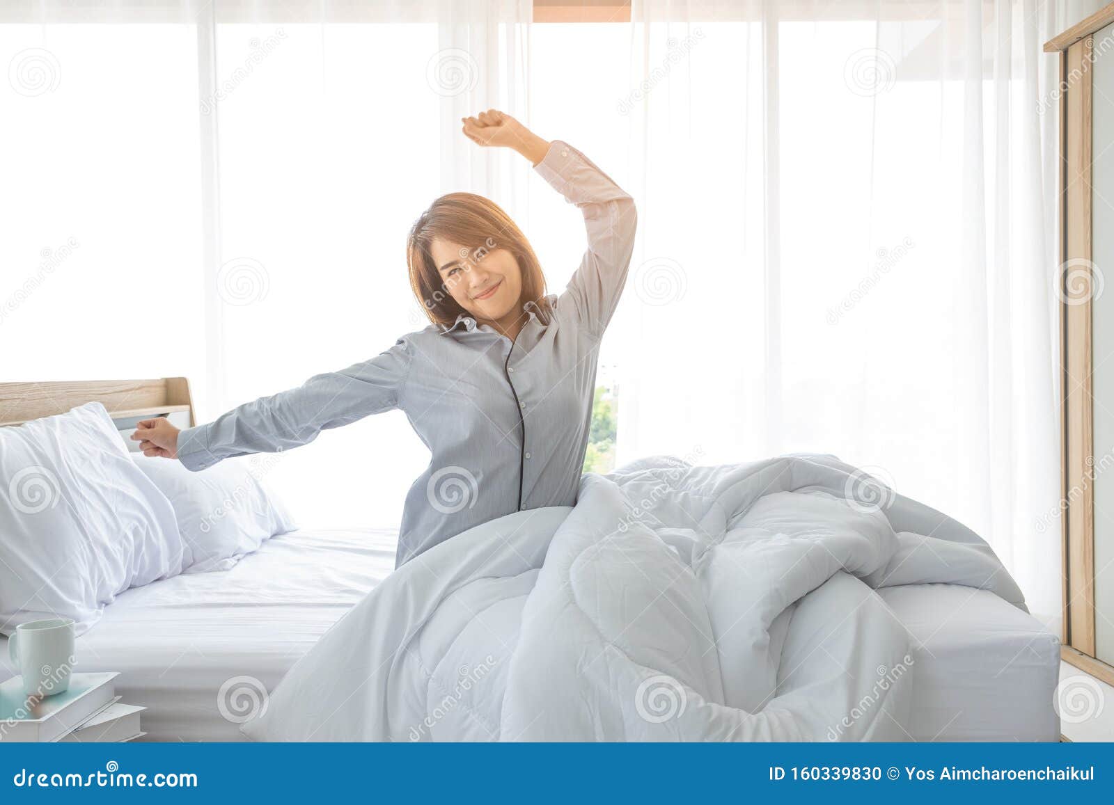 an asian woman aged about 20 wakes up in the morning in a bright bed in a bedroom or hotel after a restful night`s sleep