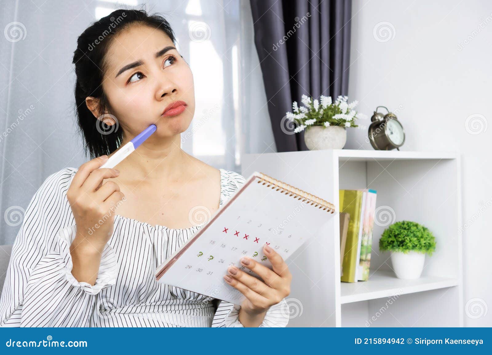 asian woman hand holding calendar and pregnancy test counting the date and checking her menstrual cycle planning for ovulation