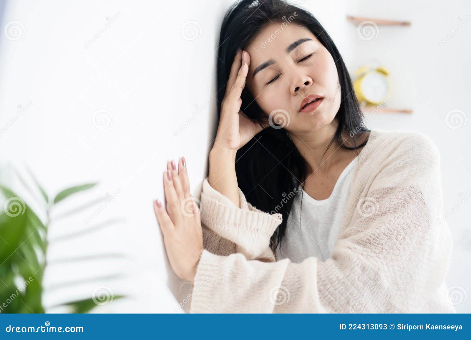 asian woman having problem with meniere`s disease, fainting or dizziness hand holding her head leaning against the wall