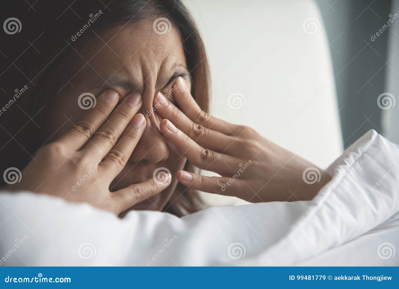 asian woman rubbing eyes with her hands on her bed.
