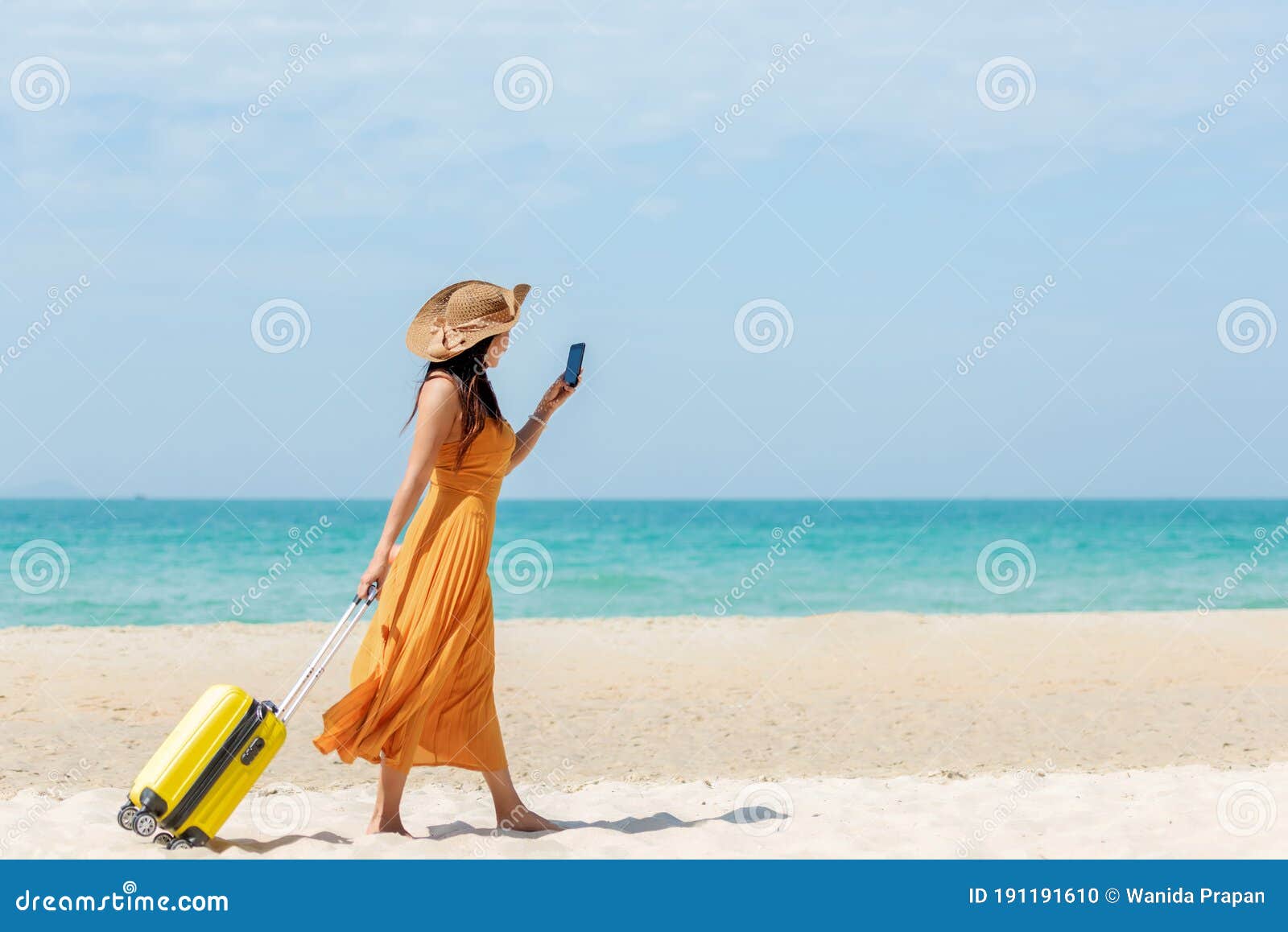 asian women traveler holding yellow luggage walking and check in smart phone on the beach