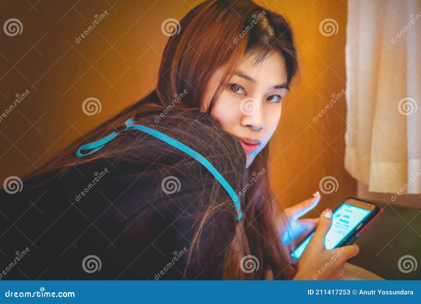 Asian Woman Using Mobile Phone On The Bed While Turn Around And Looking At The Camera Stock