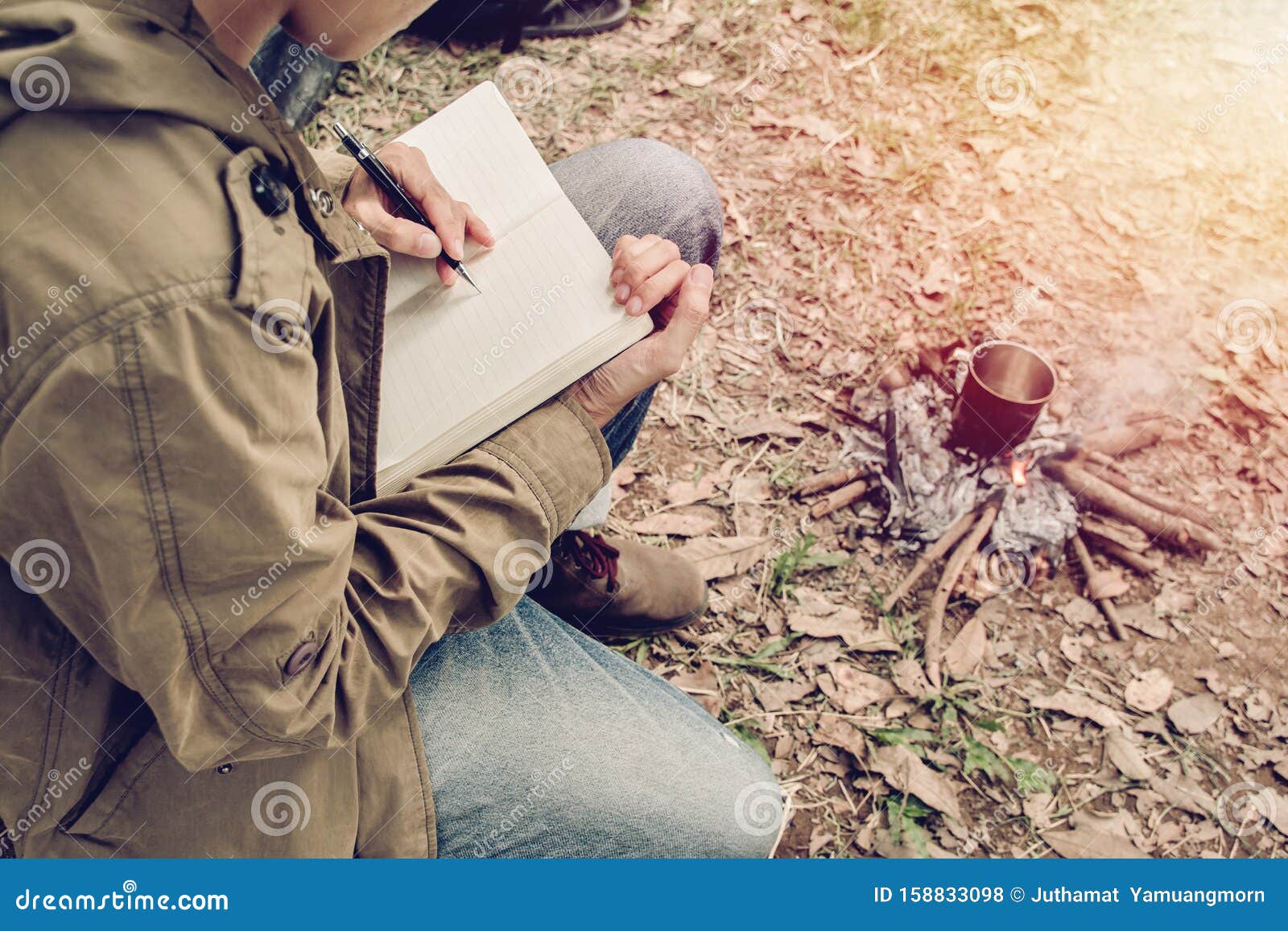 asian young man sitting is holding a pen writing note of letter memorize memories on book in outside the tent. loneliness camping