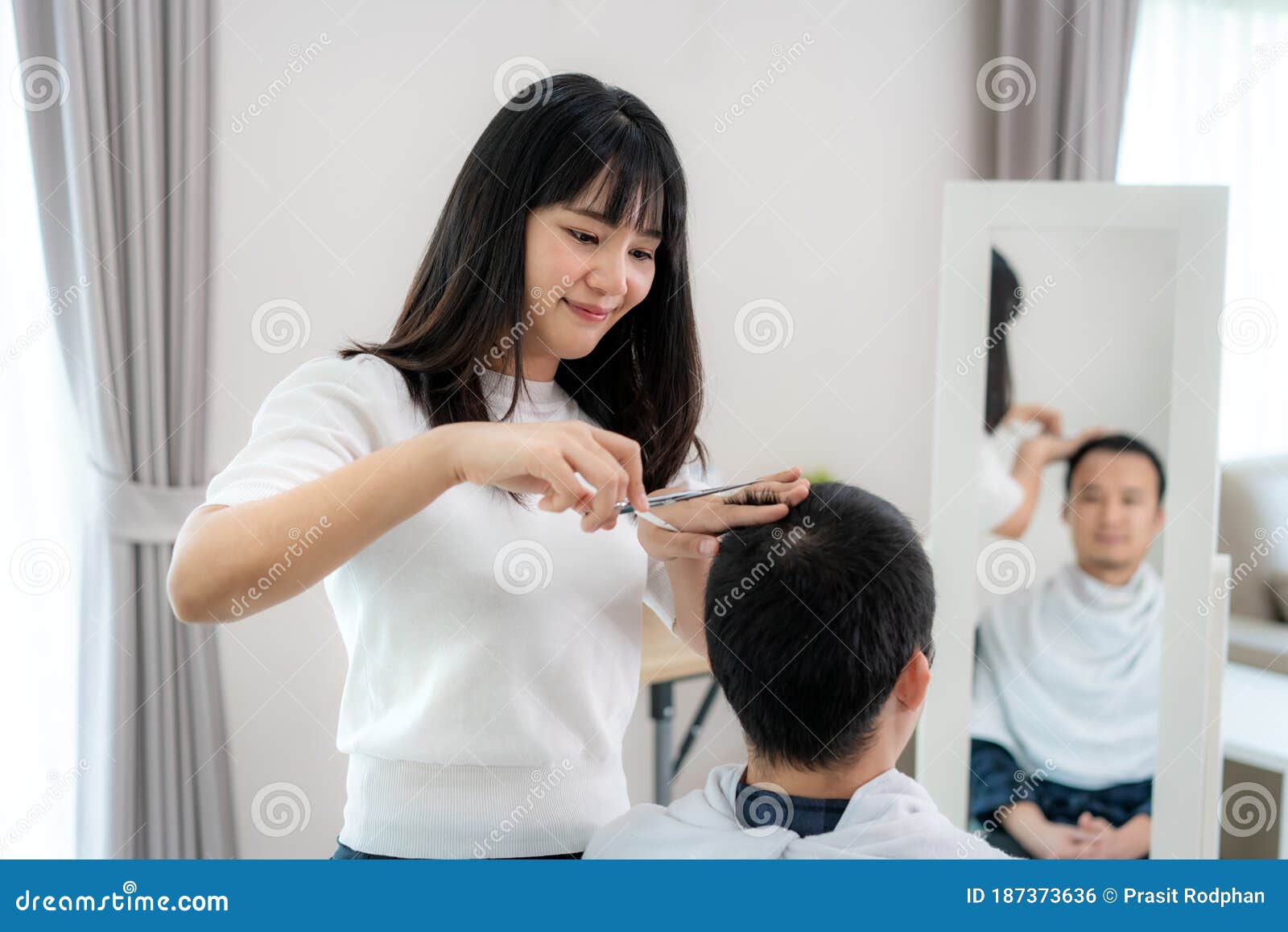 asian young man with her girlfriend hairdresser cutting hair with haircutting scissors at home they stay at home during time of