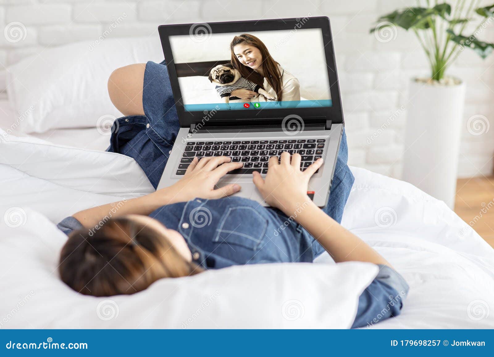 asian young woman lying on bed and using computer laptop vdo call conference to meeting friend