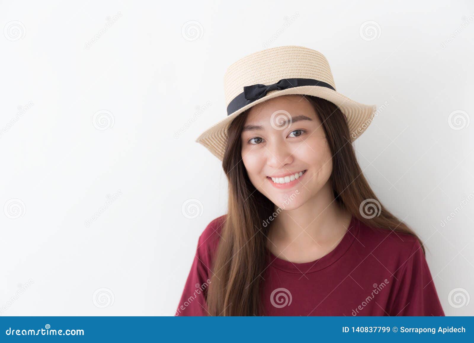 Asiatisches Mädchen, das ein rotes Hemd, stehend trägt, auf einem weißen Hintergrund lächelnd