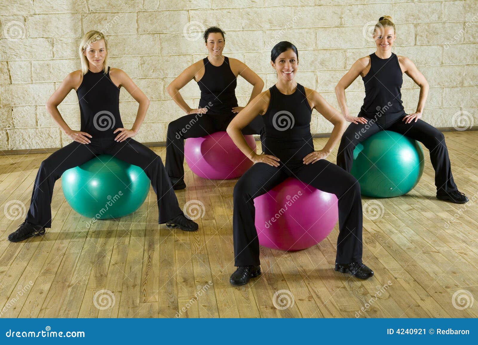 Asiento suave. Un grupo de mujeres que hacen el ejercicio que se sienta en bolas grandes. Son sonrientes y de miradas de la cámara. Vista delantera.