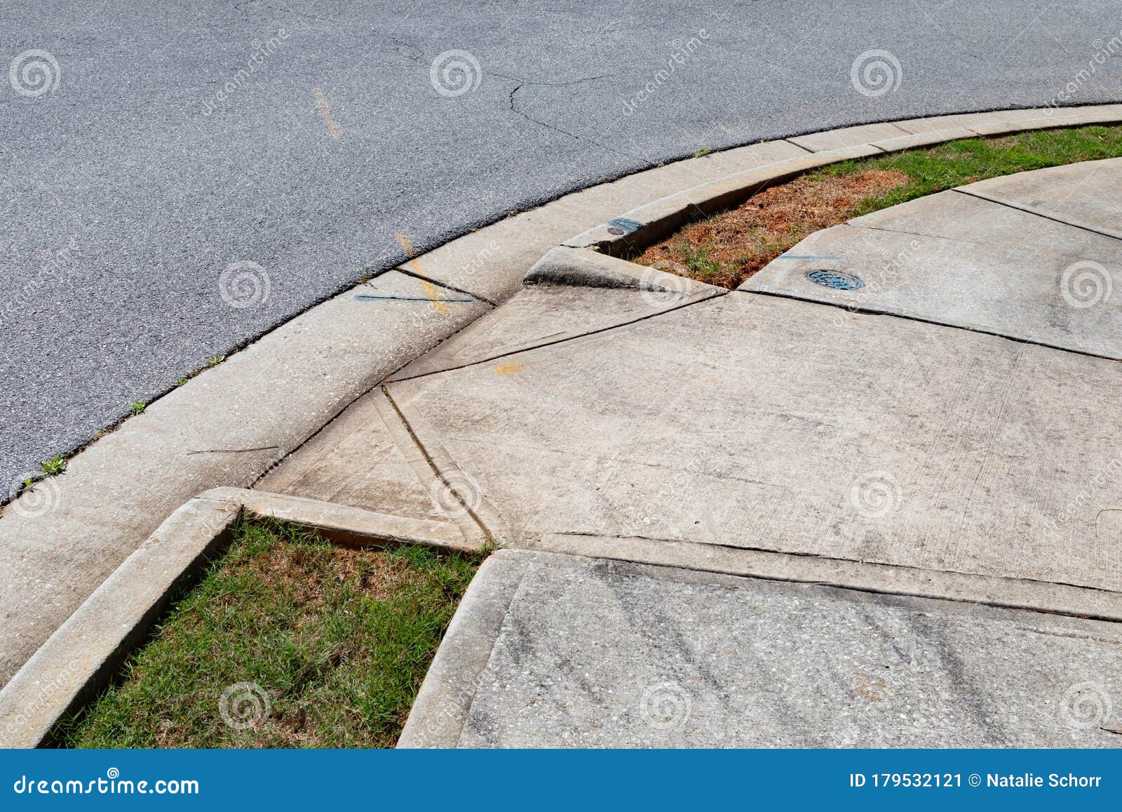 asphalt street and concrete sidewalk with graded ramp between, green grass