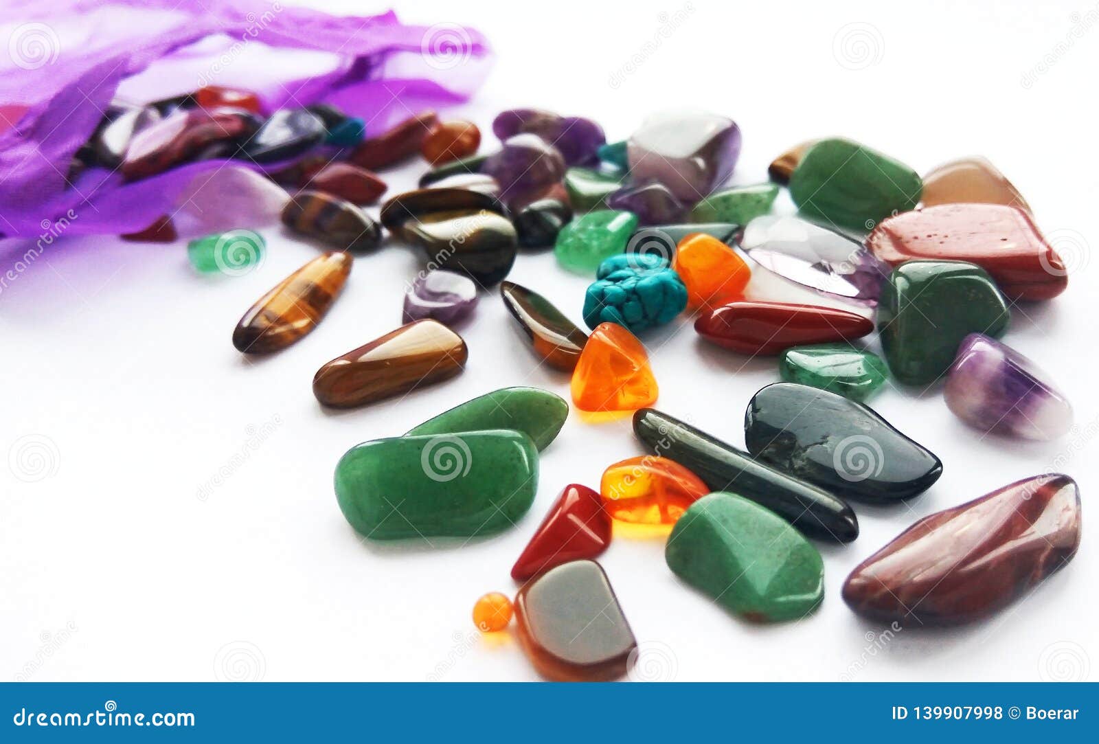natural bright coloured semi precious gemstones and gems with a bag on white background