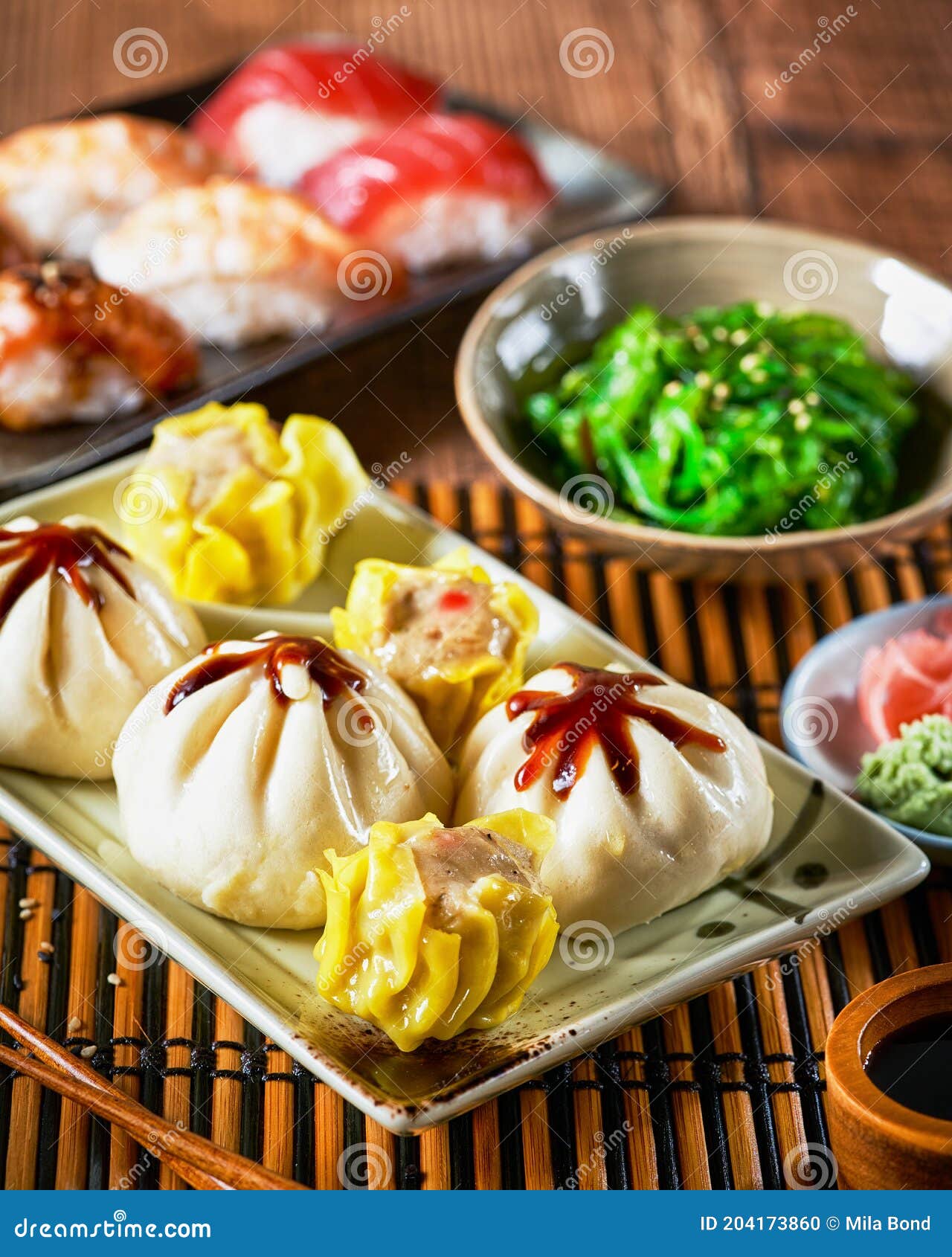 assortment of japanese sushi set, xiao long bao, shaomoi, nigiri, gyozas dumplings and wakame salad in ceramic plates with soy