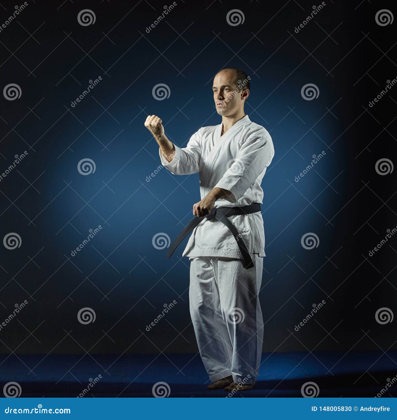 Athlete Performs Formal Karate Exercises on a Blue Tatami Stock Photo