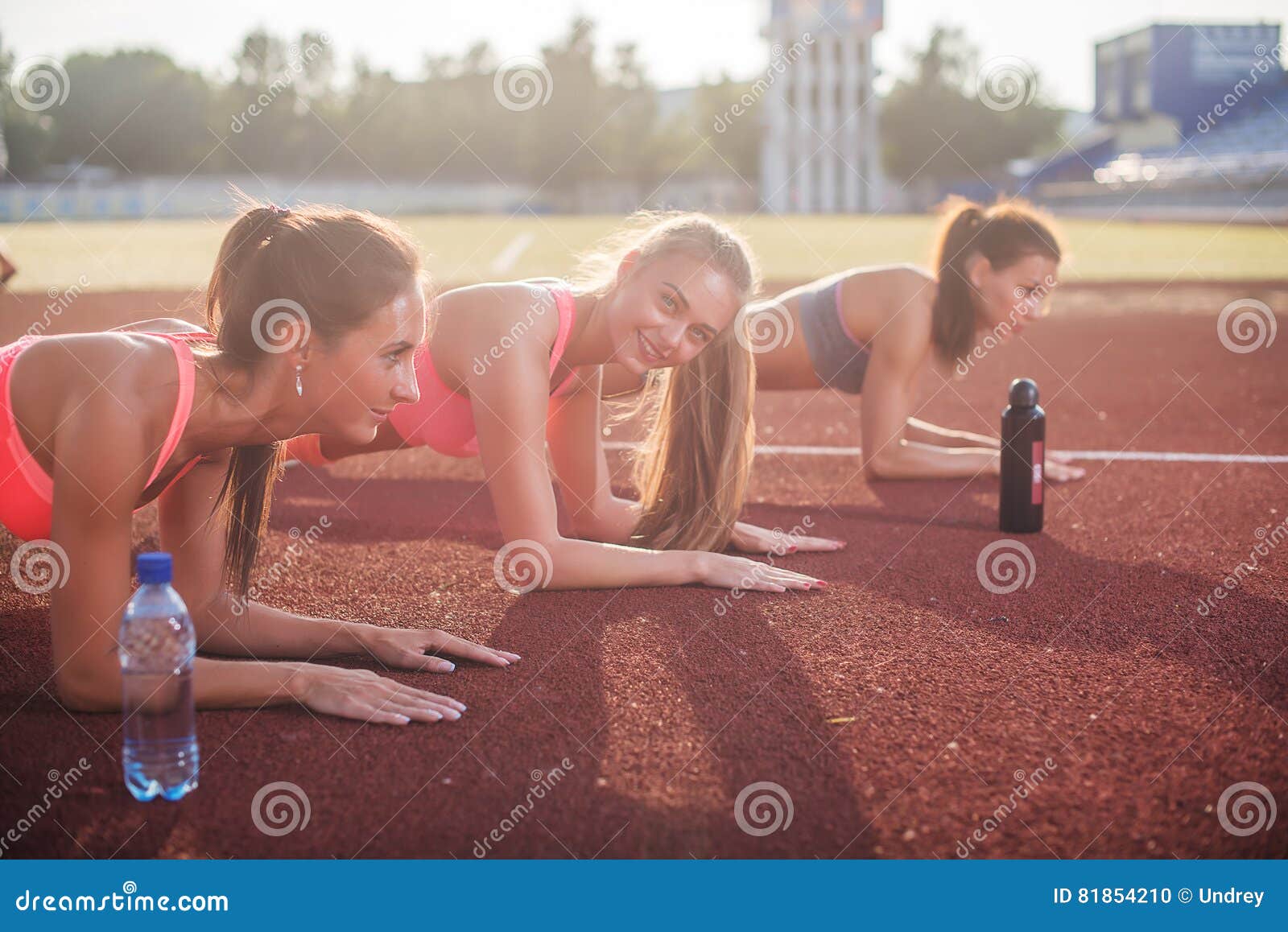 athletic group of women training on a sunny day doing planking exercise in the stadium.