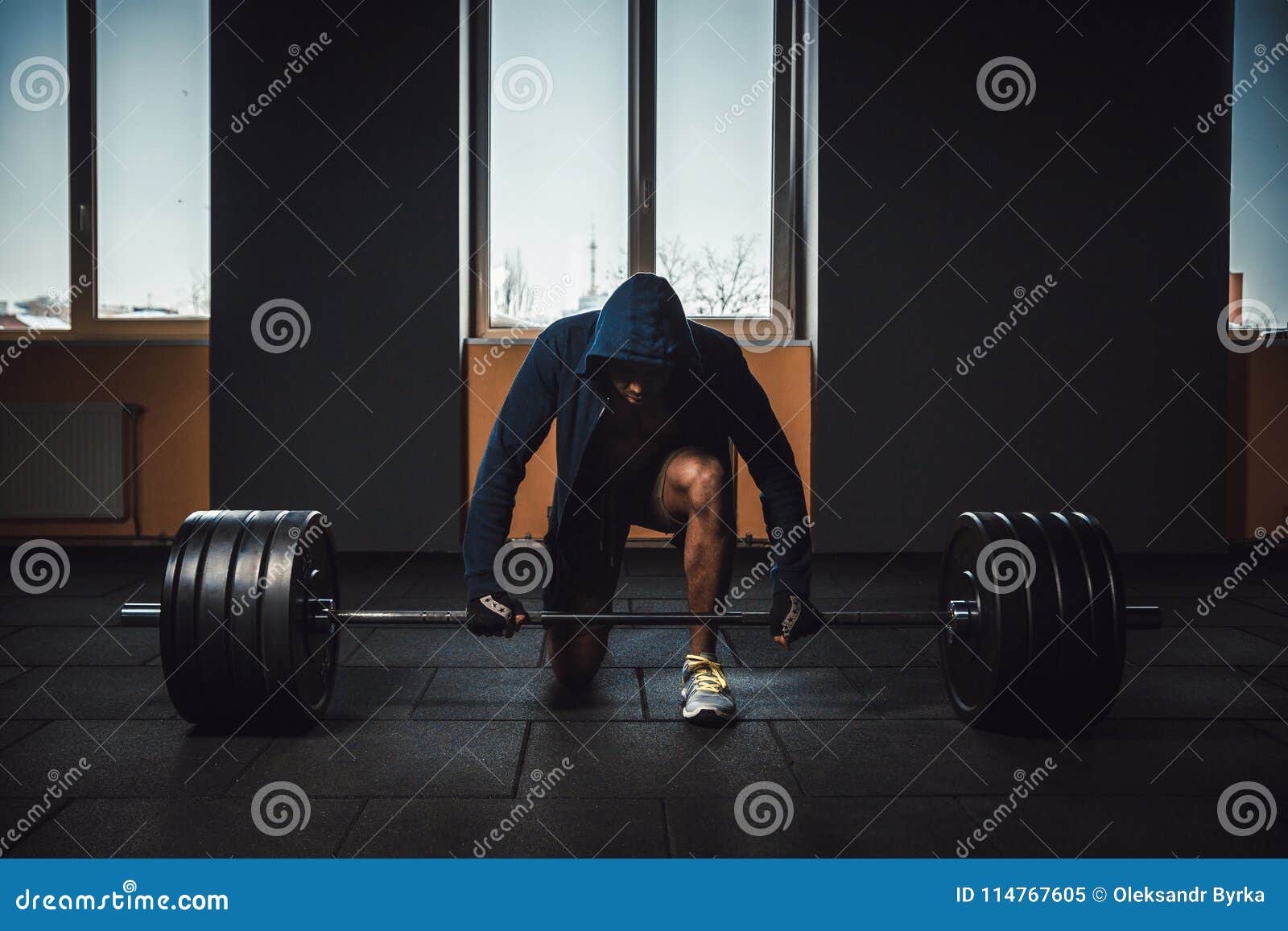 athletic man in jacket with a hood waiting and preparing before lifting heavy barbell. fitness, sport, training, gym and lifestyle