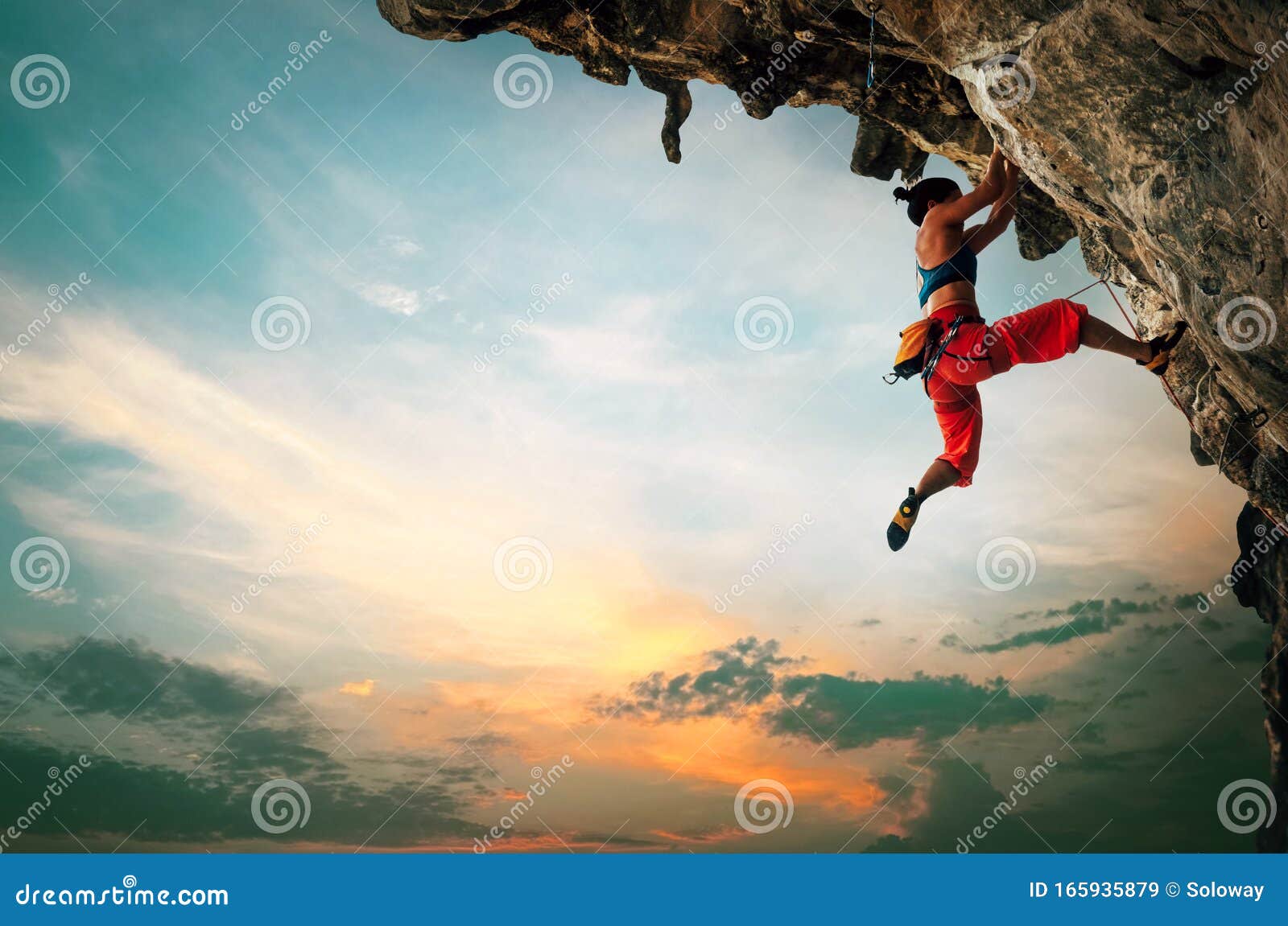 athletic woman climbing on overhanging cliff rock with sunset sky background