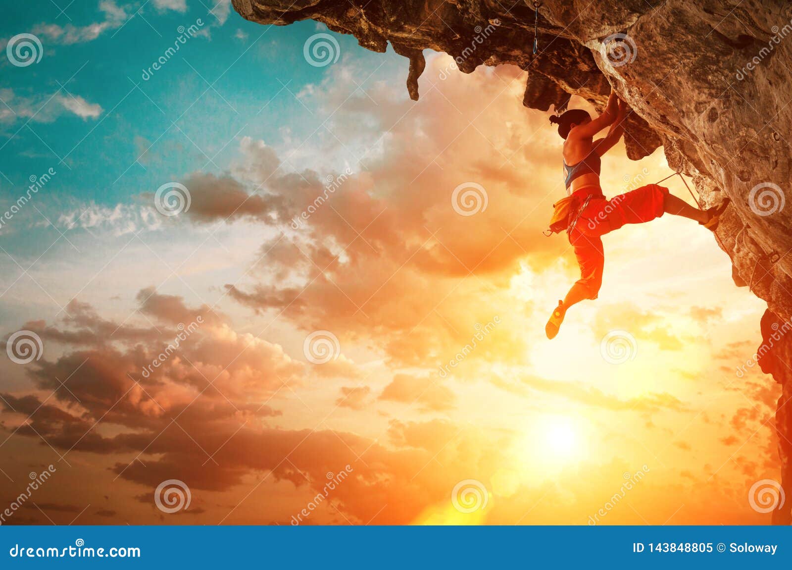 athletic woman climbing on overhanging cliff rock with sunset sky background
