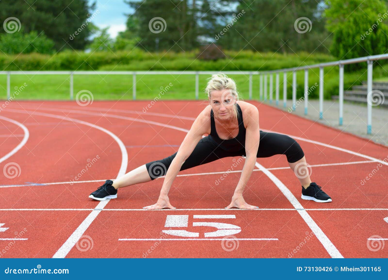 athletic woman doing straddle stretches on track