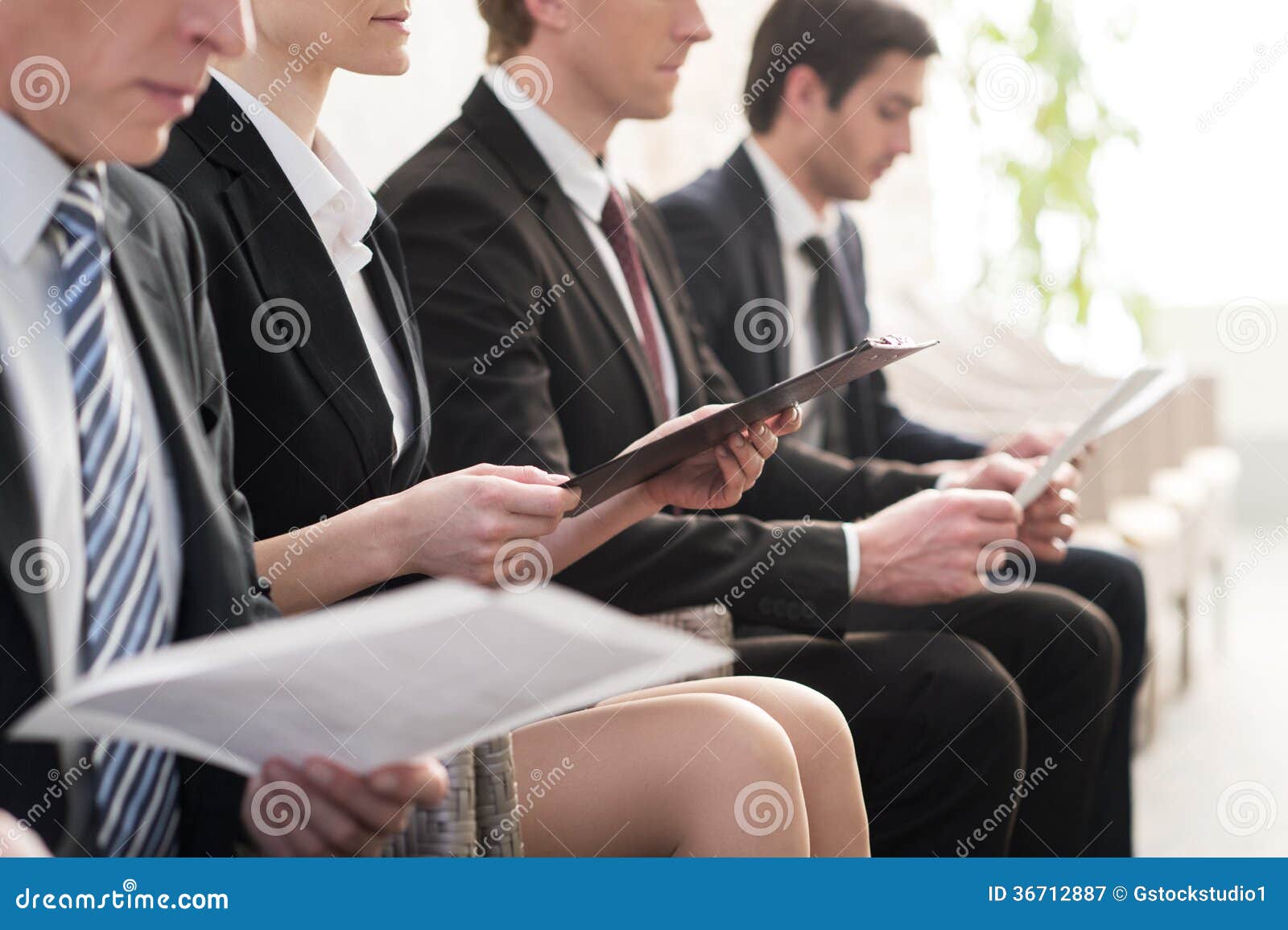 Attente dans la ligne. Image cultivée des personnes dans le formalwear attendant dans la ligne tout en se reposant aux chaises et tenant des papiers dans leurs mains