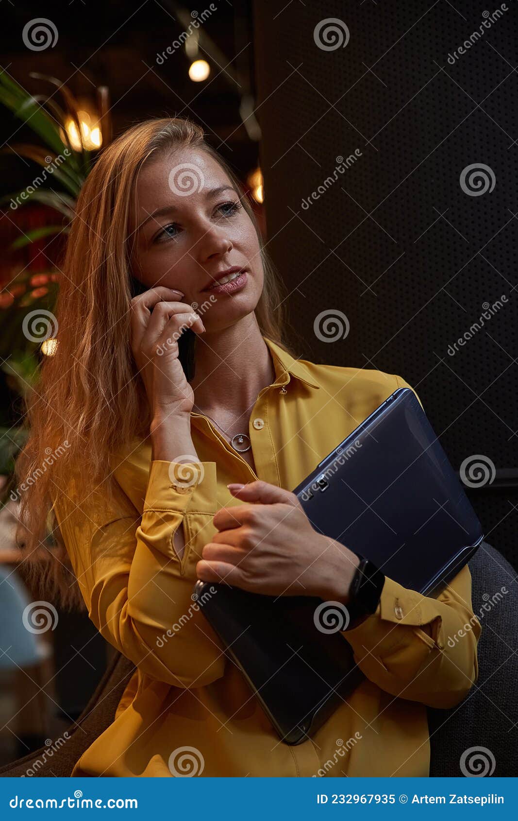 attractive cauasian woman calling by smartphone, holding laptop in hands at cafe