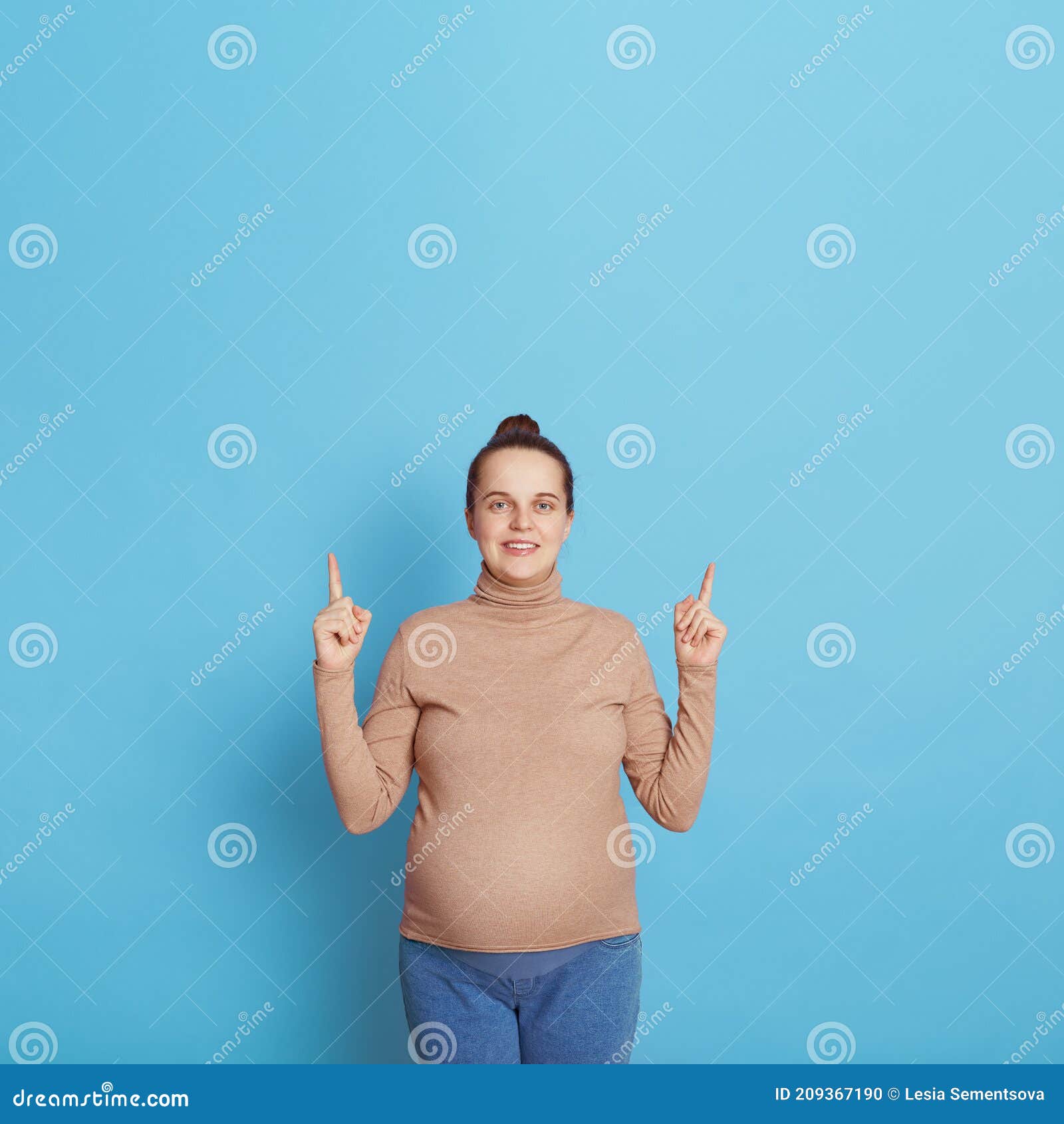 Attractive European Pregnant Woman Pointing Finger Up With Both Index Fingers Looks At Camera