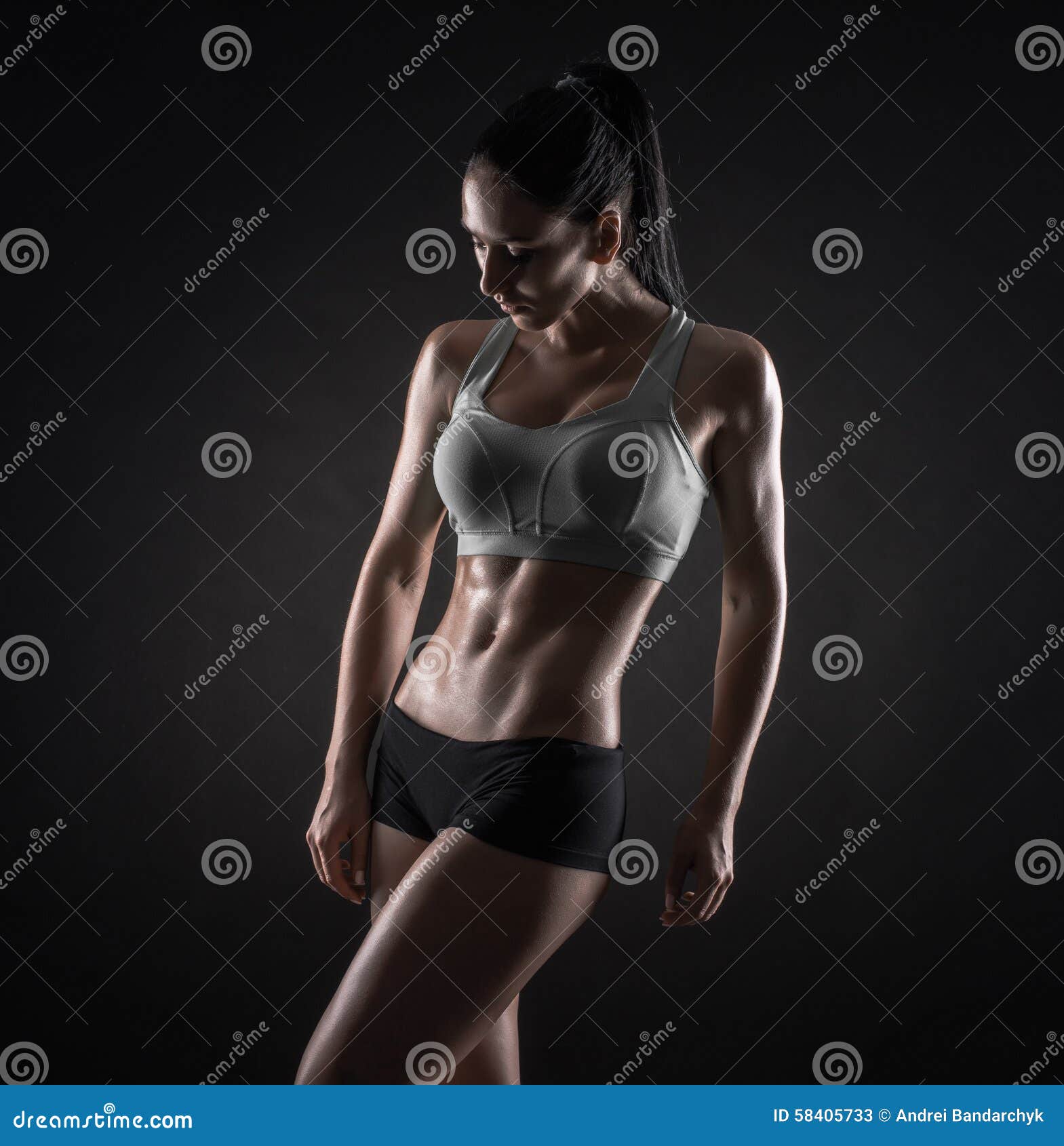 Young athletic woman in sportswear posing in studio against black  background. Ideal female sports figure. Fitness girl with perfect sculpted  muscular and tight body. Stock Photo