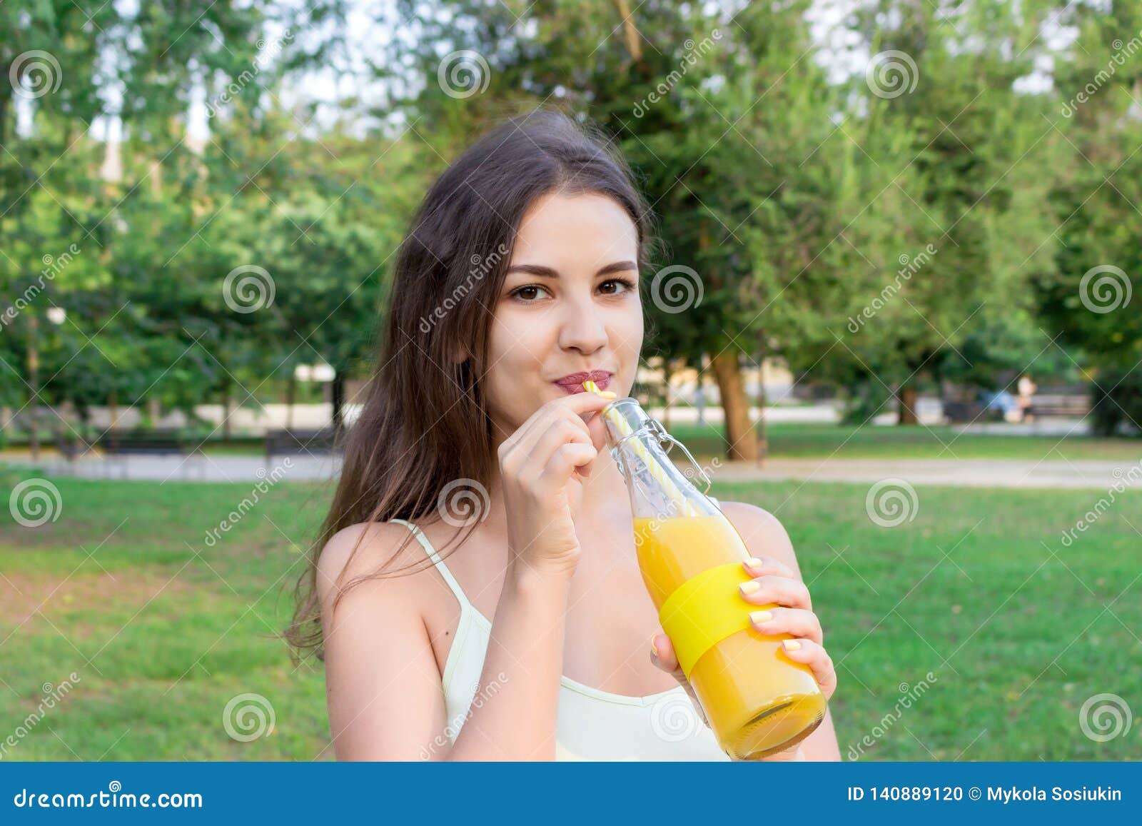 Attractive Girl Is Drinking Fresh Juice Through The Straw Outdoors Pretty Woman Is Holding A