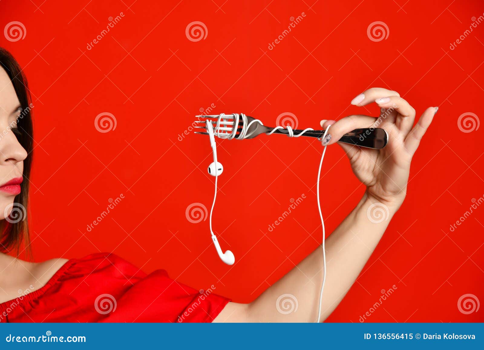 Attractive girl in red dress holding a fork in hands. on the headphone plug. prepared to eat. Music saturation