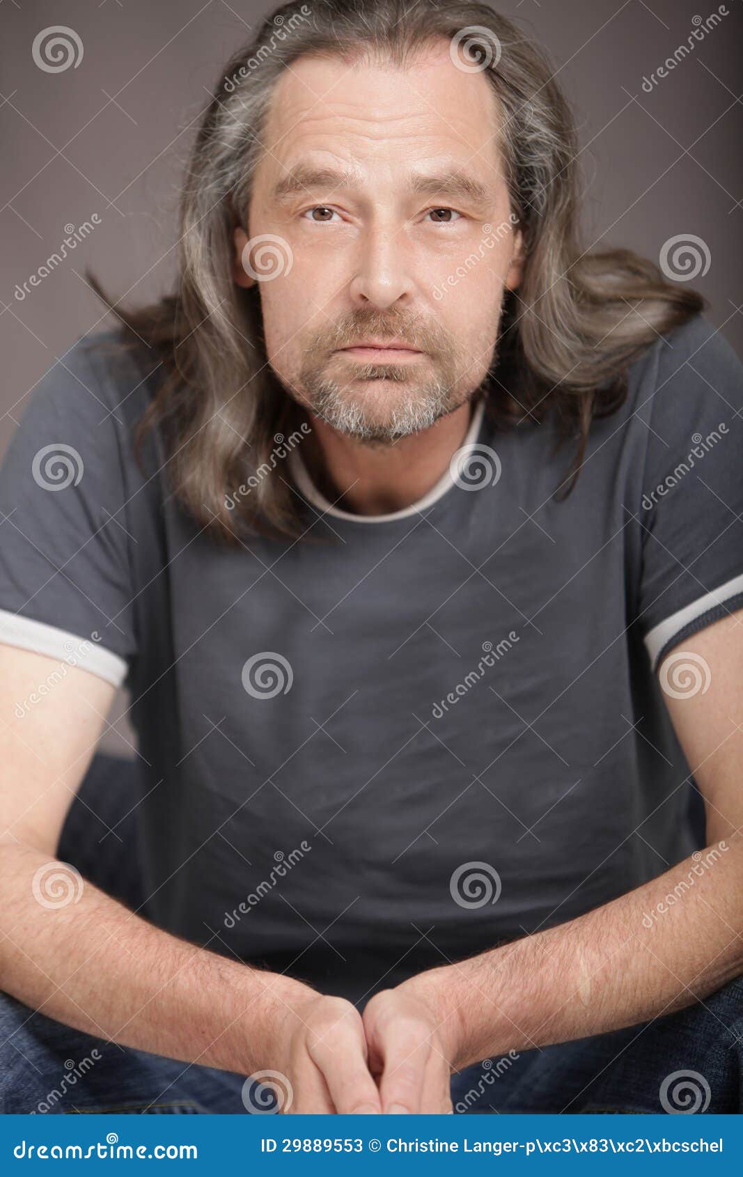 attractive middle aged man beard long hair sitting chair facing camera serious expression 29889553