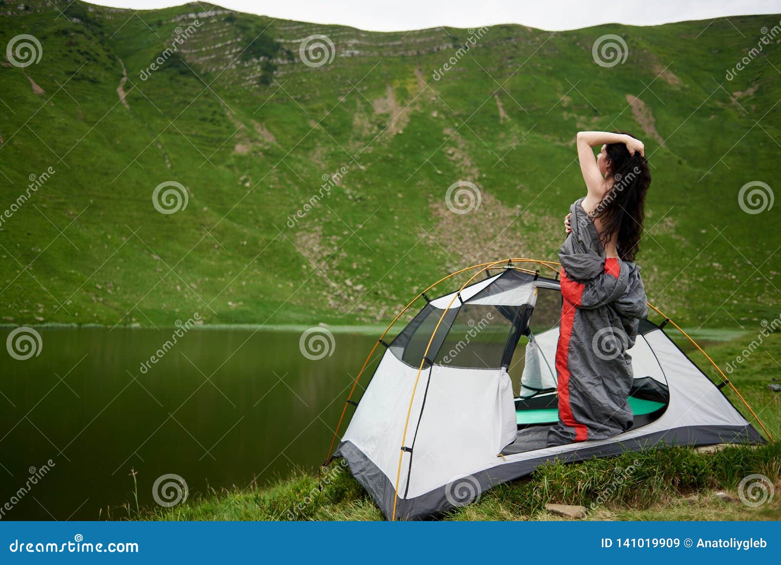 Hiking woman stops near lake in mountains, carries backback, holds thermos  of hot beverage, explores Stock Photo by wayhomestudioo