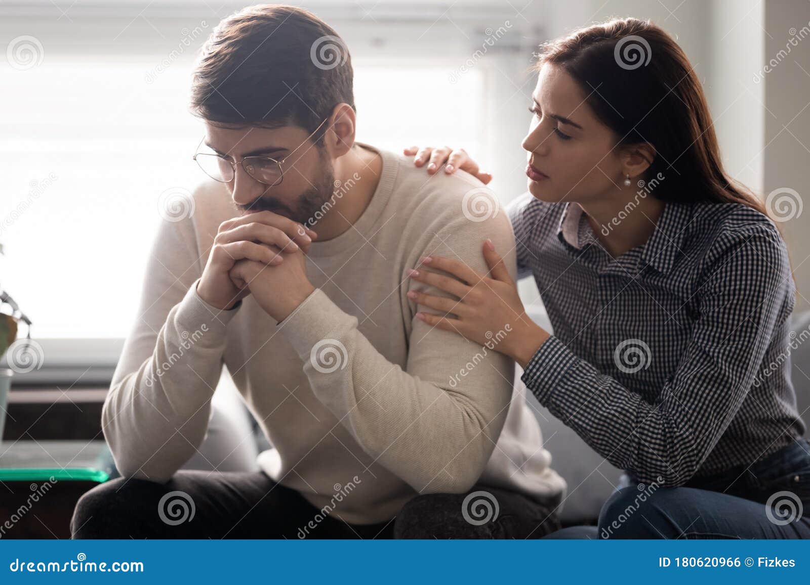  A concerned wife comforts her upset husband by putting a hand on his shoulder.