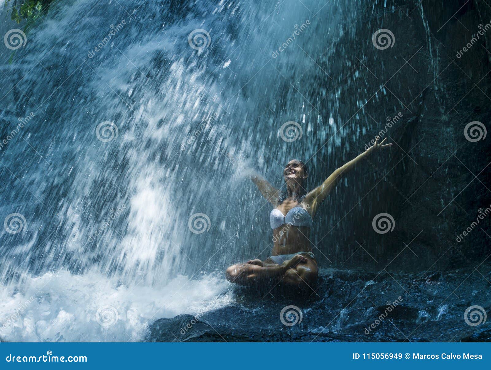 attractive woman sitting at rock in yoga pose for spiritual relaxation serenity and meditation at stunning beautiful waterfall and