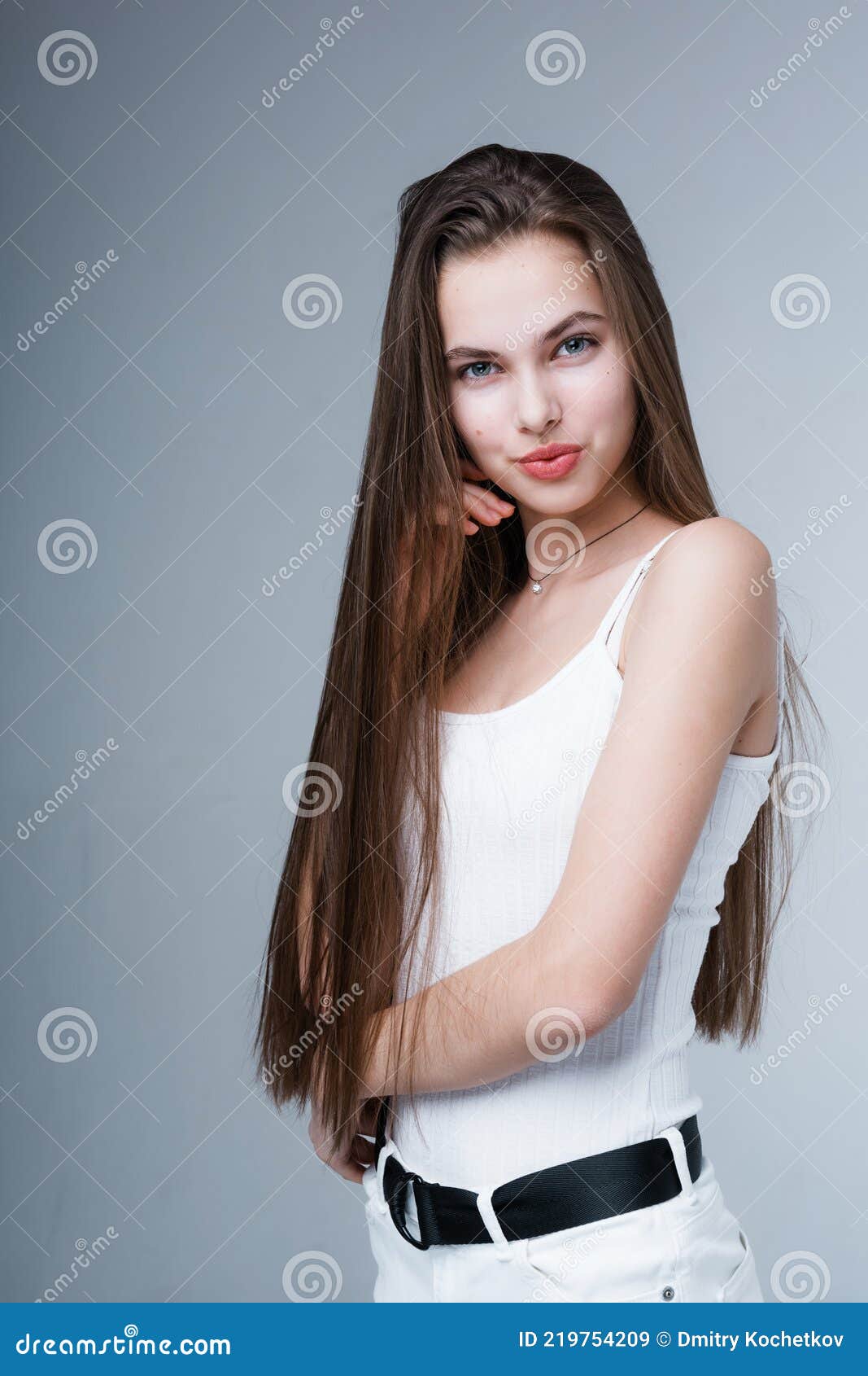 attractive young girl in a white tank top and trousers with long shiny hair stands sideways and looks at the camera