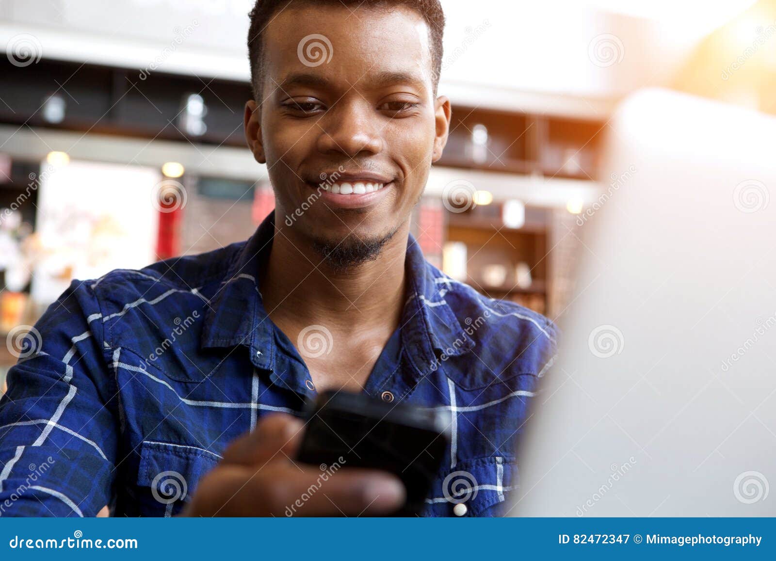 attractive young man with cellphone and laptop in cafe