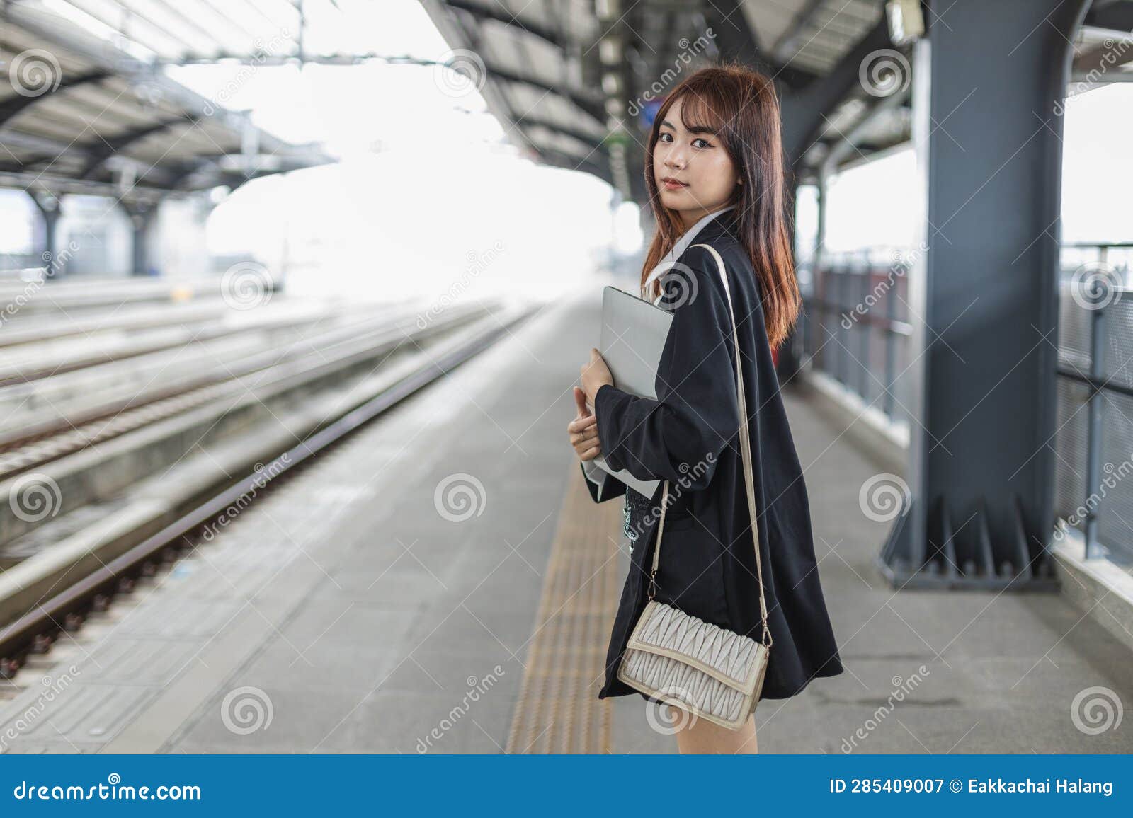 attractive young woman in black suit holding laptop smiling looking a camera standing at public places. lifestyle people