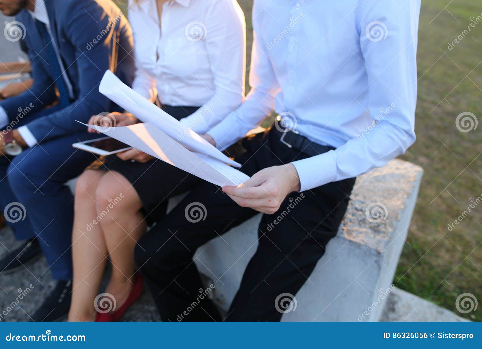 Attraktive überzeugte Leute, zwei Jungen und zwei Mädchen, entrepreneu. Junge zeitgenössische überzeugte Leute, zwei Jungen und zwei Mädchen, die Perspektivenunternehmer, die Studenten, die, mit einander, unter Verwendung der Geräte, die Laptops, Tablette und Smartphone für Arbeit mit Büroprogrammen plaudernd, Unternehmensplan aufstellend lächeln, besprechen sich, Momente, Anteil Arbeits von Geschäftsideen, lösen die Probleme und draußen sitzen auf Geländer Einer von Kerlen kleidete im blauen klassischen Anzug, im weißen Hemd mit Bindung, in den zweiten Männern, die im hellblauen Hemd und in der schwarzen formalen Hose gekleidet wurden, im Mädchen mit dem gelockten Haar, in den Gläsern und in rotem Lippenstift, die in der weißen Bluse und im schwarzen Rock, das blonde Mädchen gekleidet wurde, das im schwarzen Kleid gekleidet wurde an Konzept des Geschäftstreffens, Gerät, Technologie, Lösen von Problemen, Geschäftskommunikation, erfolgreiche Leute, Abkommen, Freunde treffend