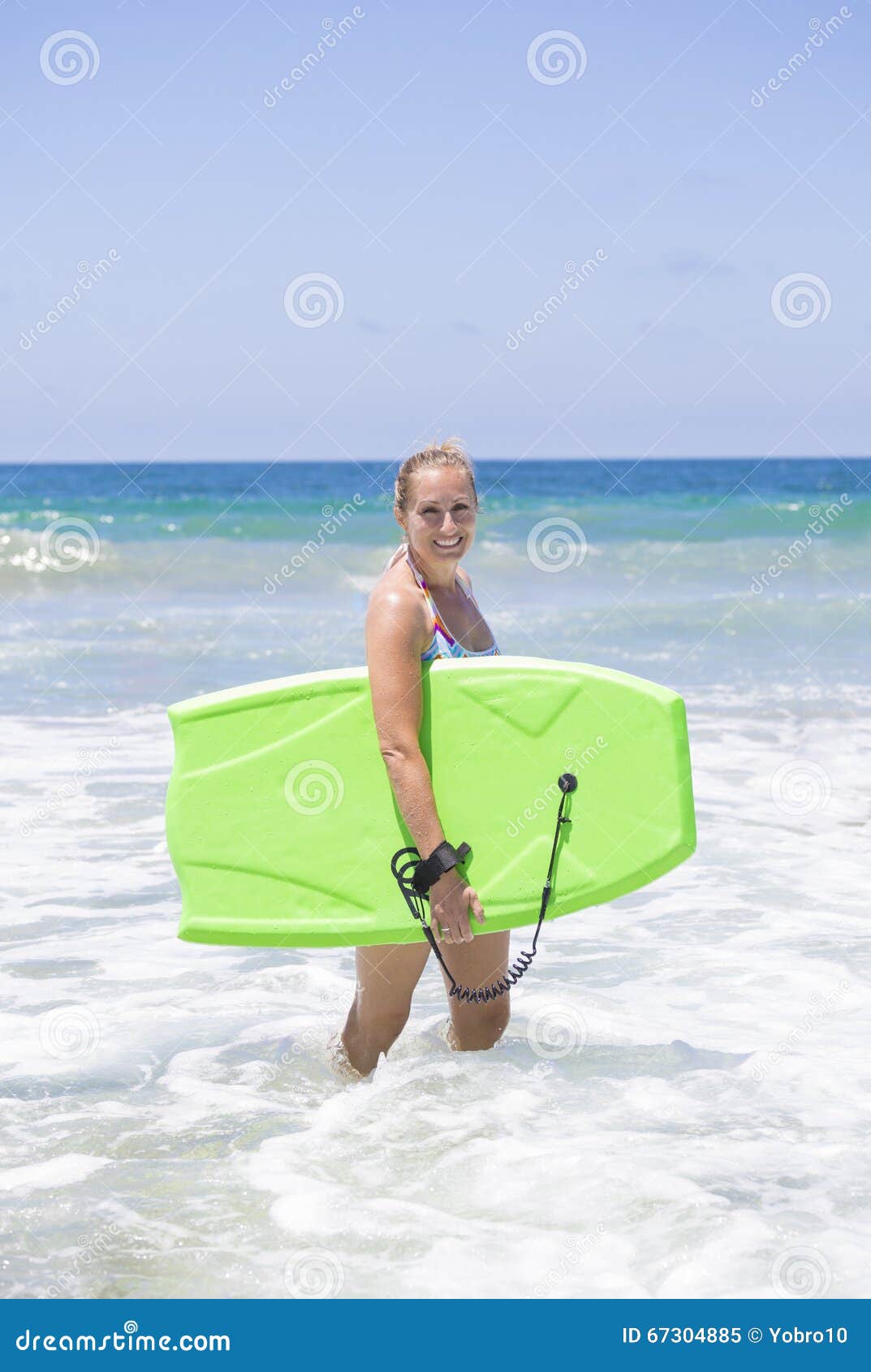 Attraktiver Frauenboogieeinstieg in den Meereswogen. Lächelnder attraktiver Frauenboogieeinstieg und Spielen in den Meereswogen Spaßtag am Strand