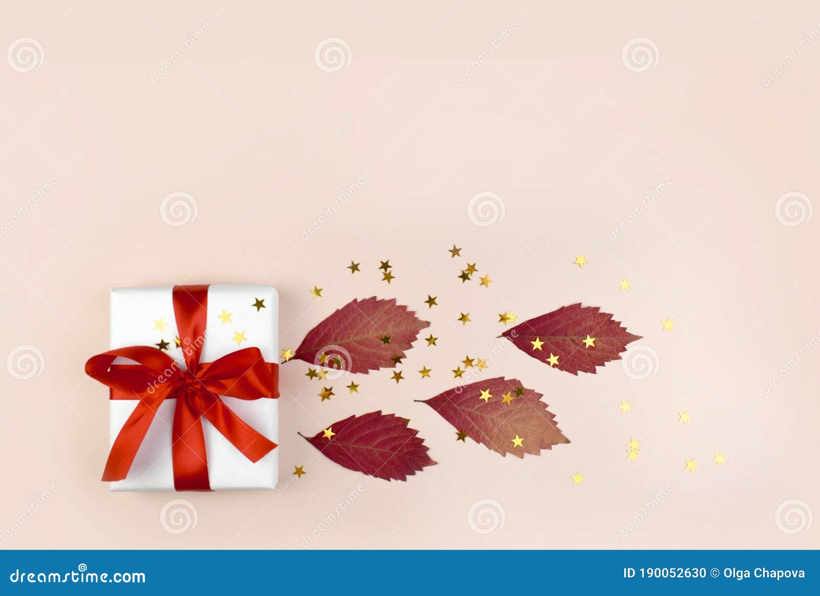 autumn composition with gift box, dried leaves and golden confetti on pastel pink backgound.