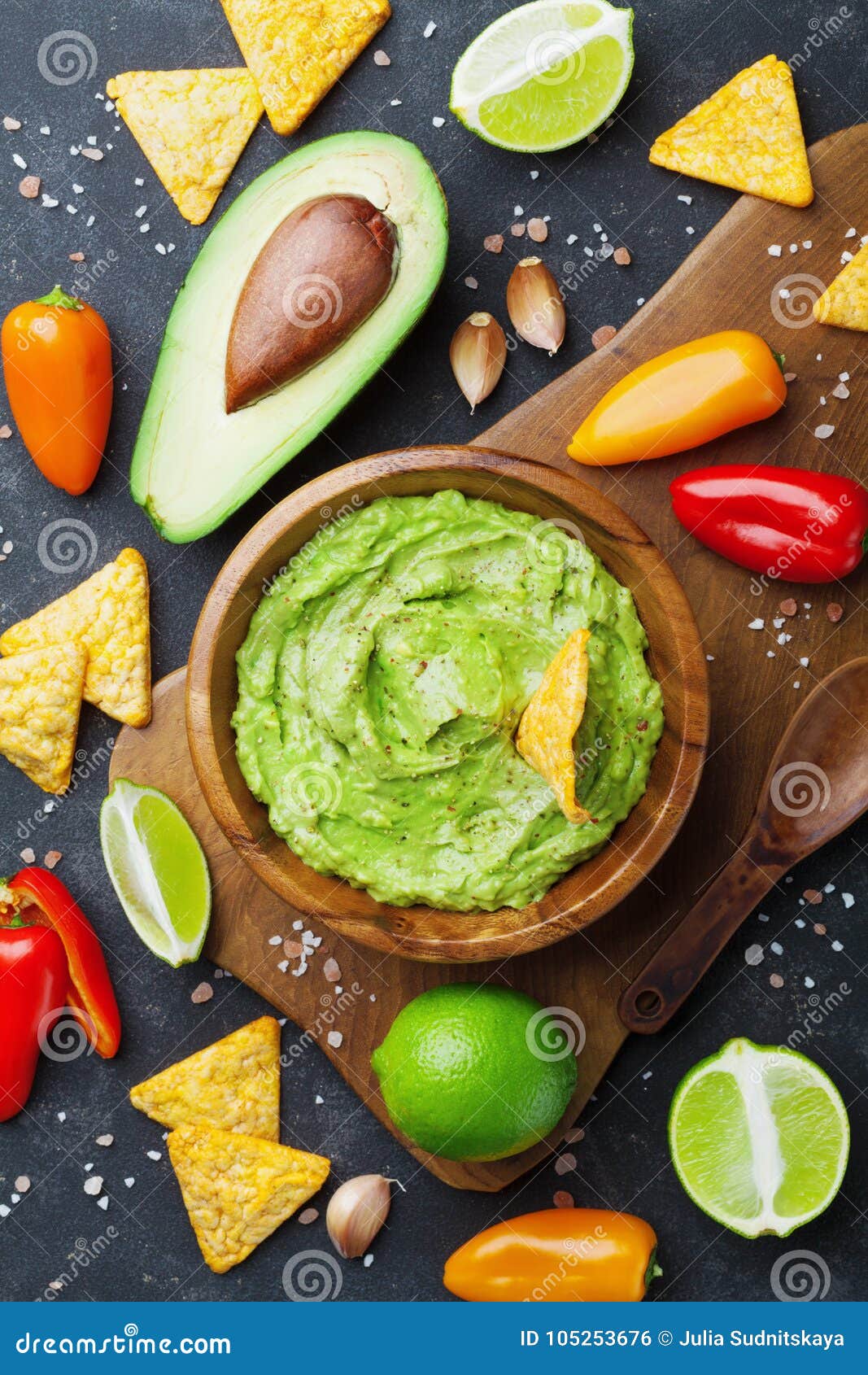 avocado guacamole with ingredients pepper, lime and nachos on black table top view. traditional mexican food.