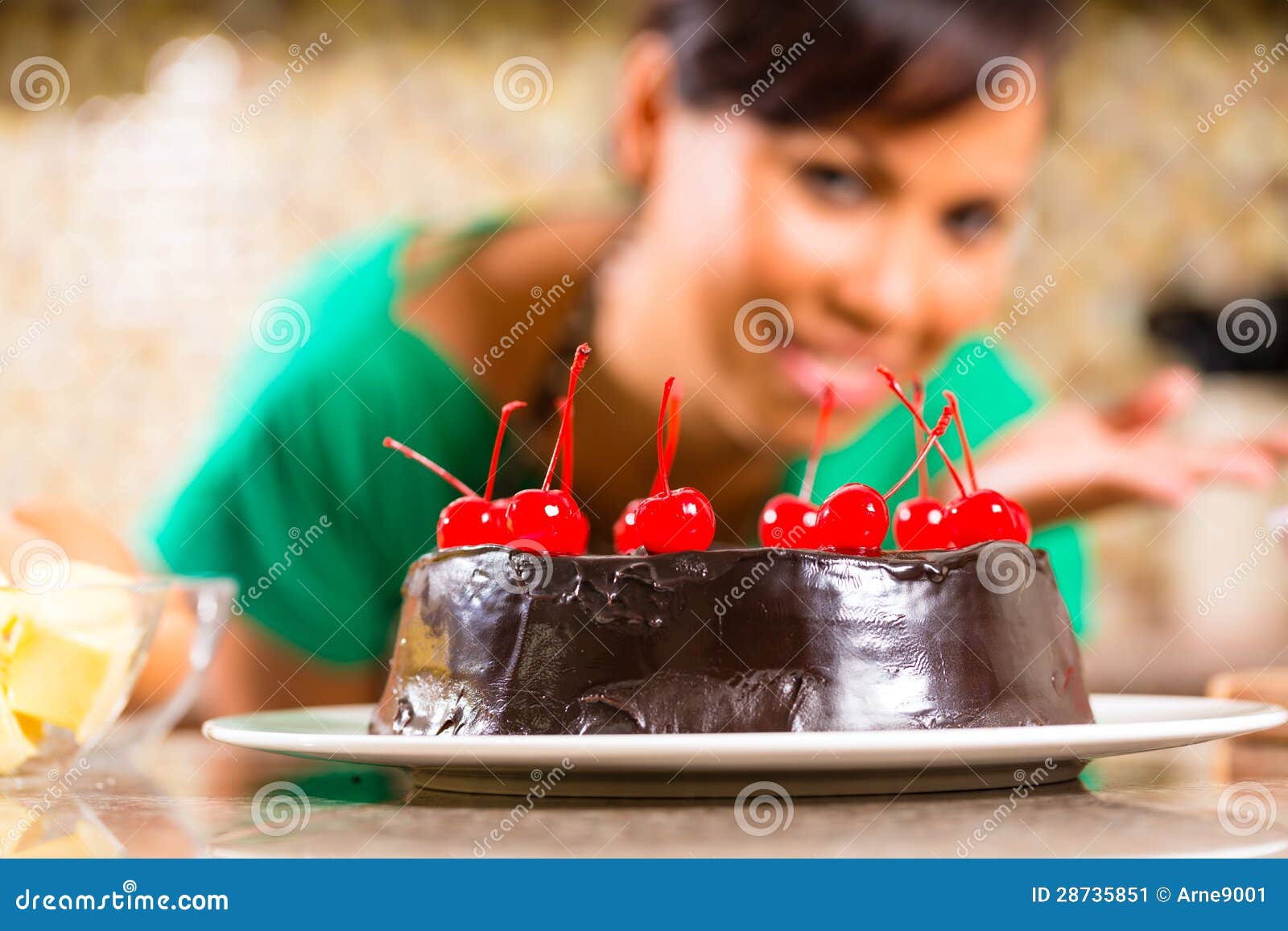 Aziatische de chocoladecake van het vrouwenbaksel in keuken. Aziatische vrouw die eigengemaakte chocoladecake met kersen voorstellen die zij in haar keuken voor dessert heeft gebakken