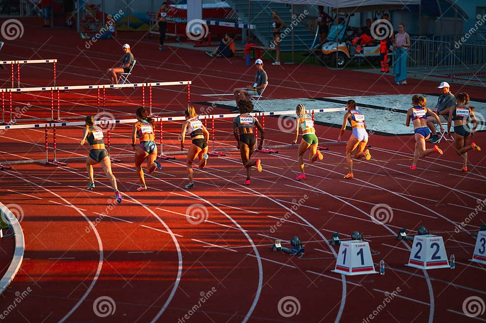 Female Sprinters Engaged in 100m Hurdles Race Athletes Compete on