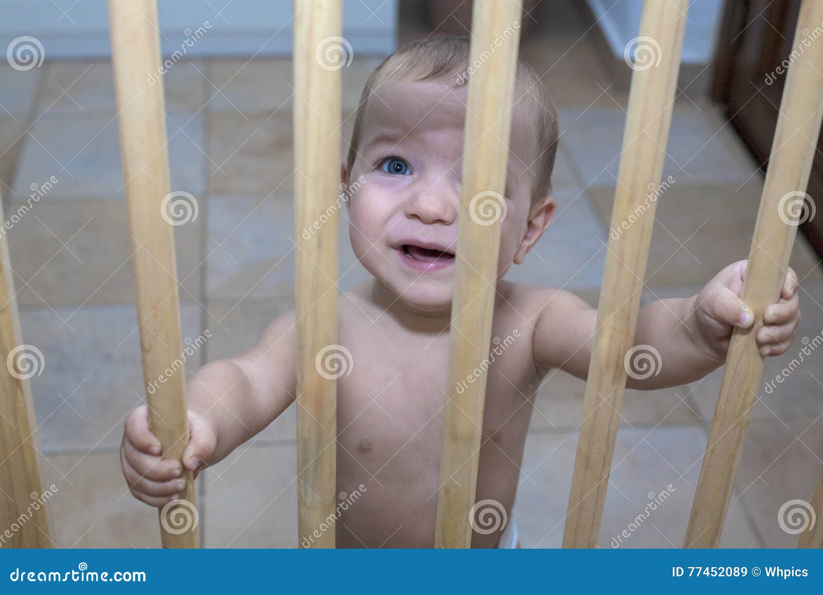 baby boy behind the wooden safety gate of stairs