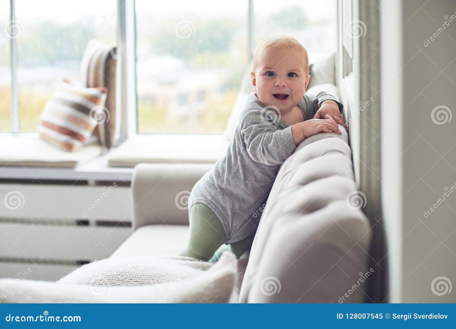 Baby Boy Crawling and Climbing on Sofa Against Big Window Stock Image