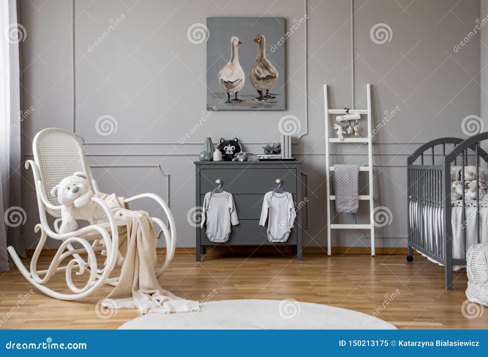 baby clothes hanging on knobs on grey wooden commode in lovely nursery, copy space and poster on empty wall