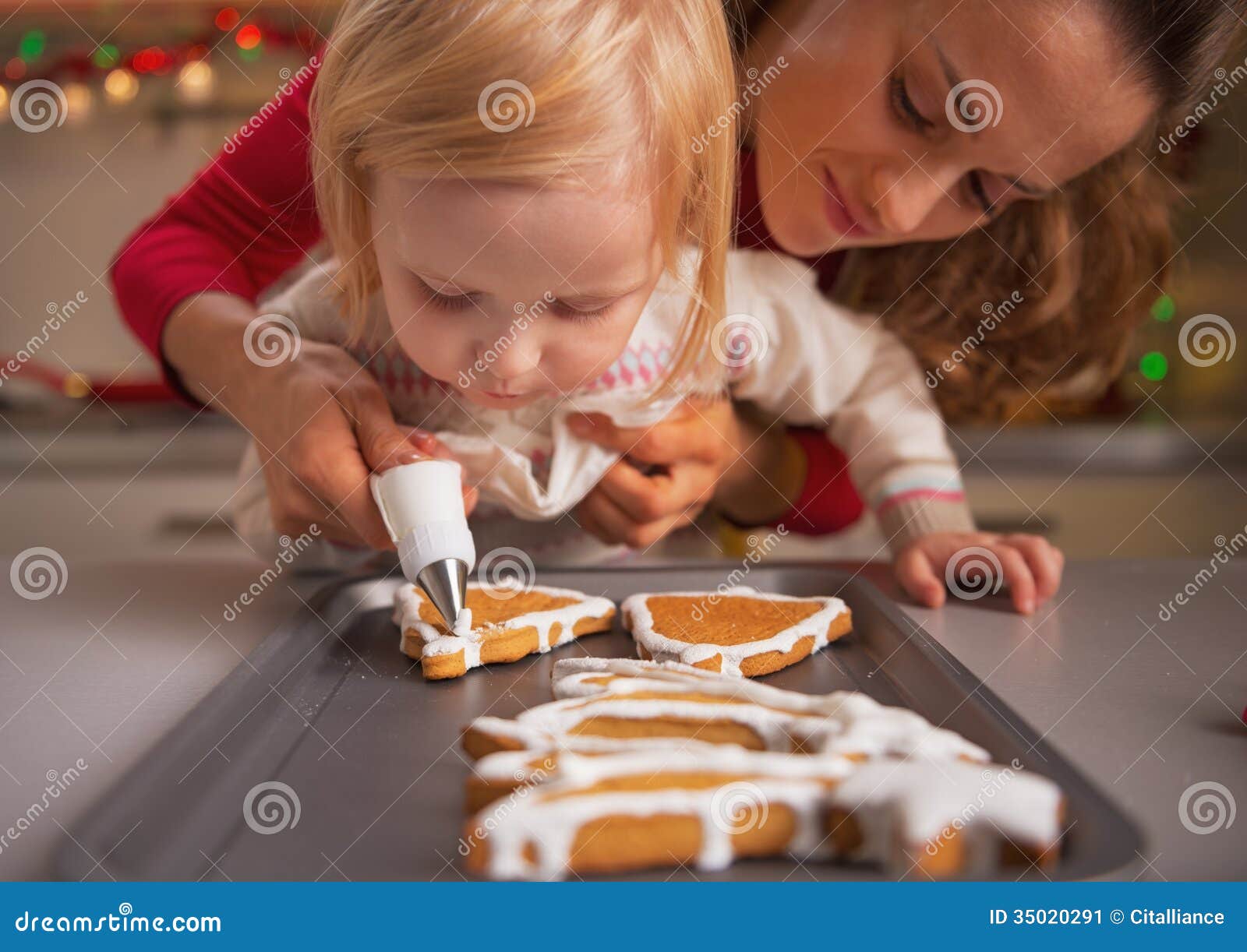 Baby die moeder helpen Kerstmiskoekjes met glans verfraaien. Baby die moeder helpen eigengemaakte Kerstmiskoekjes met glans verfraaien