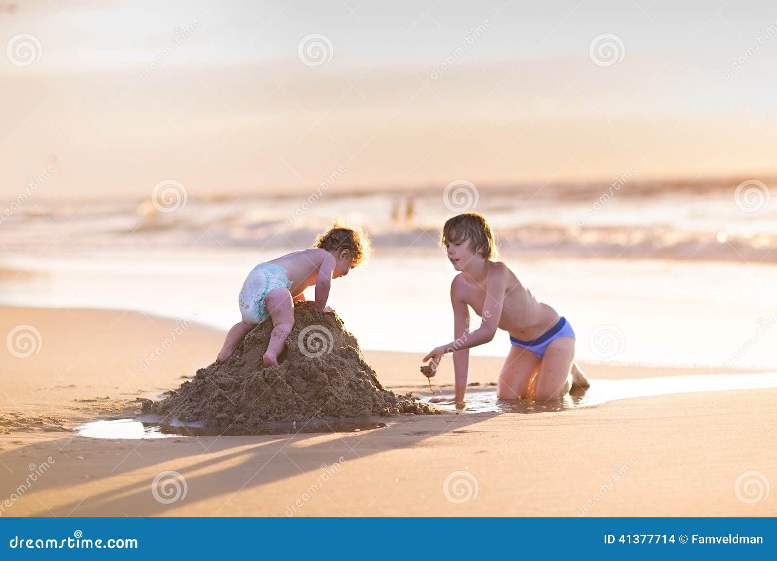 baby girl climbing sand castle her brother was builded