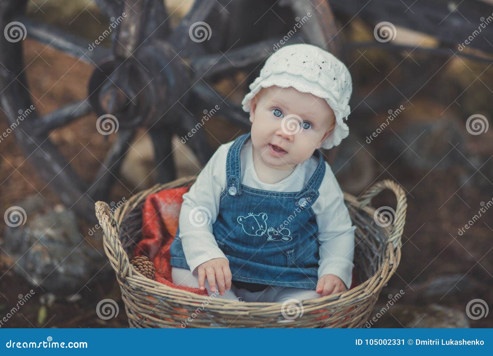 baby girl with ocean deep blue eyes and pinky cheek wearing white shirt and jeans dress and handmade craft tiny hat sitting in bas