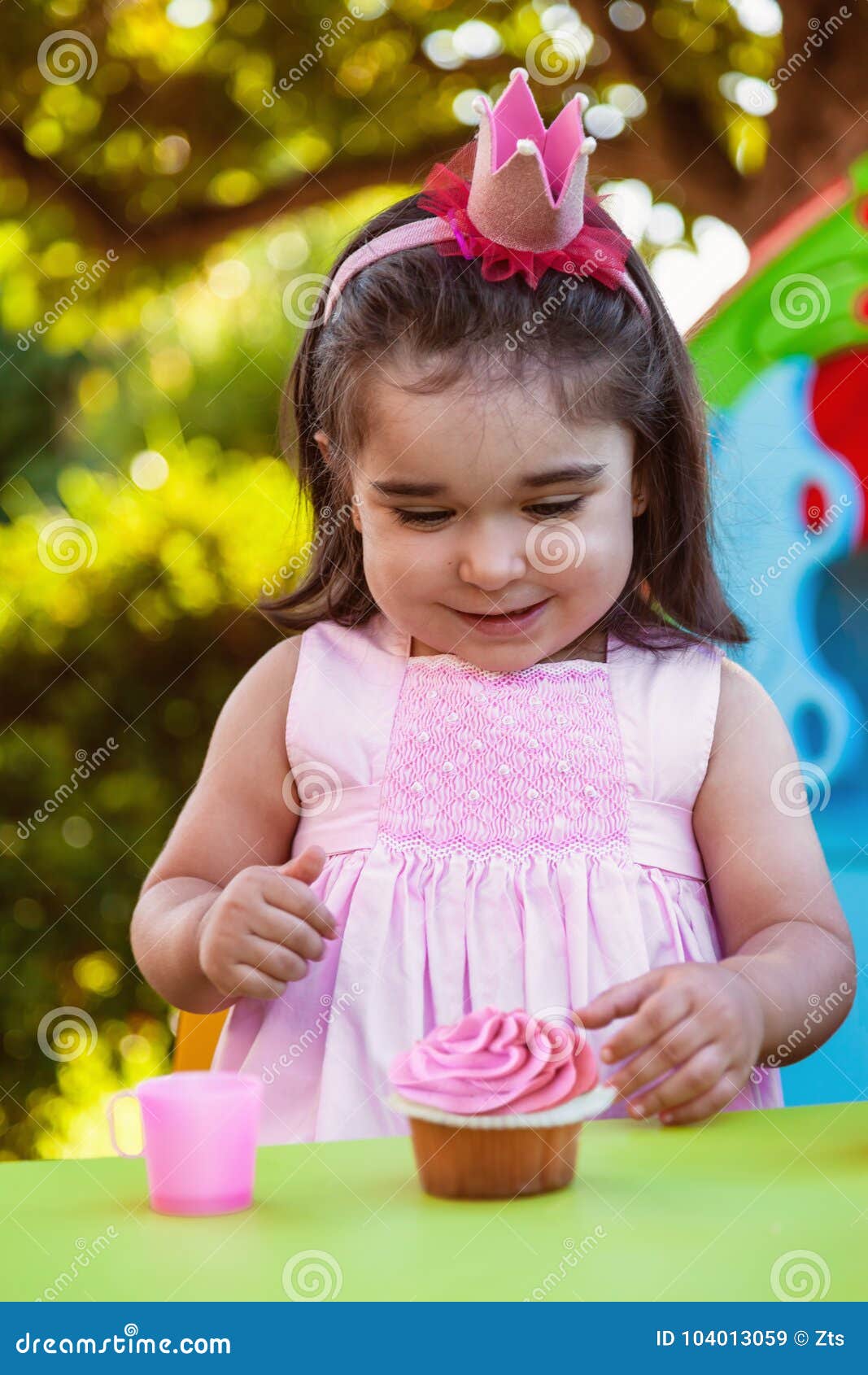 baby toddler girl in outdoor party at garden, happy and smiling at cupcake with sweet tooth expression
